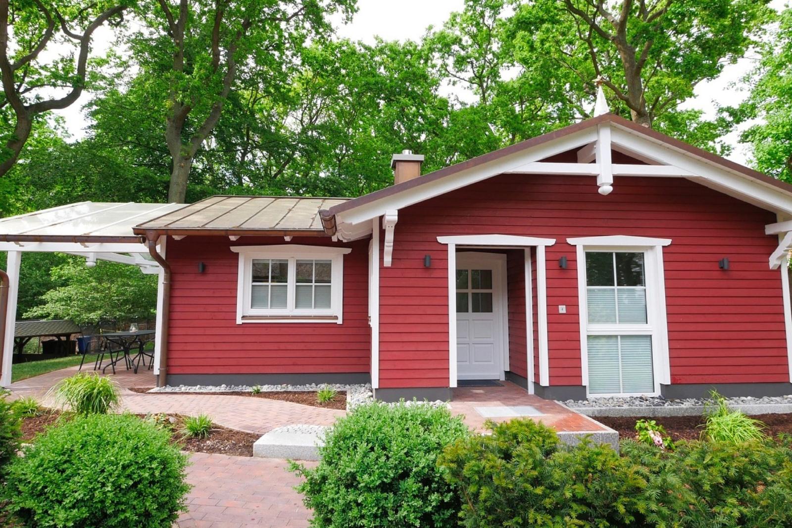 Rotes Haus mit weißen Fensterrahmen und Terrasse unter Bäumen.