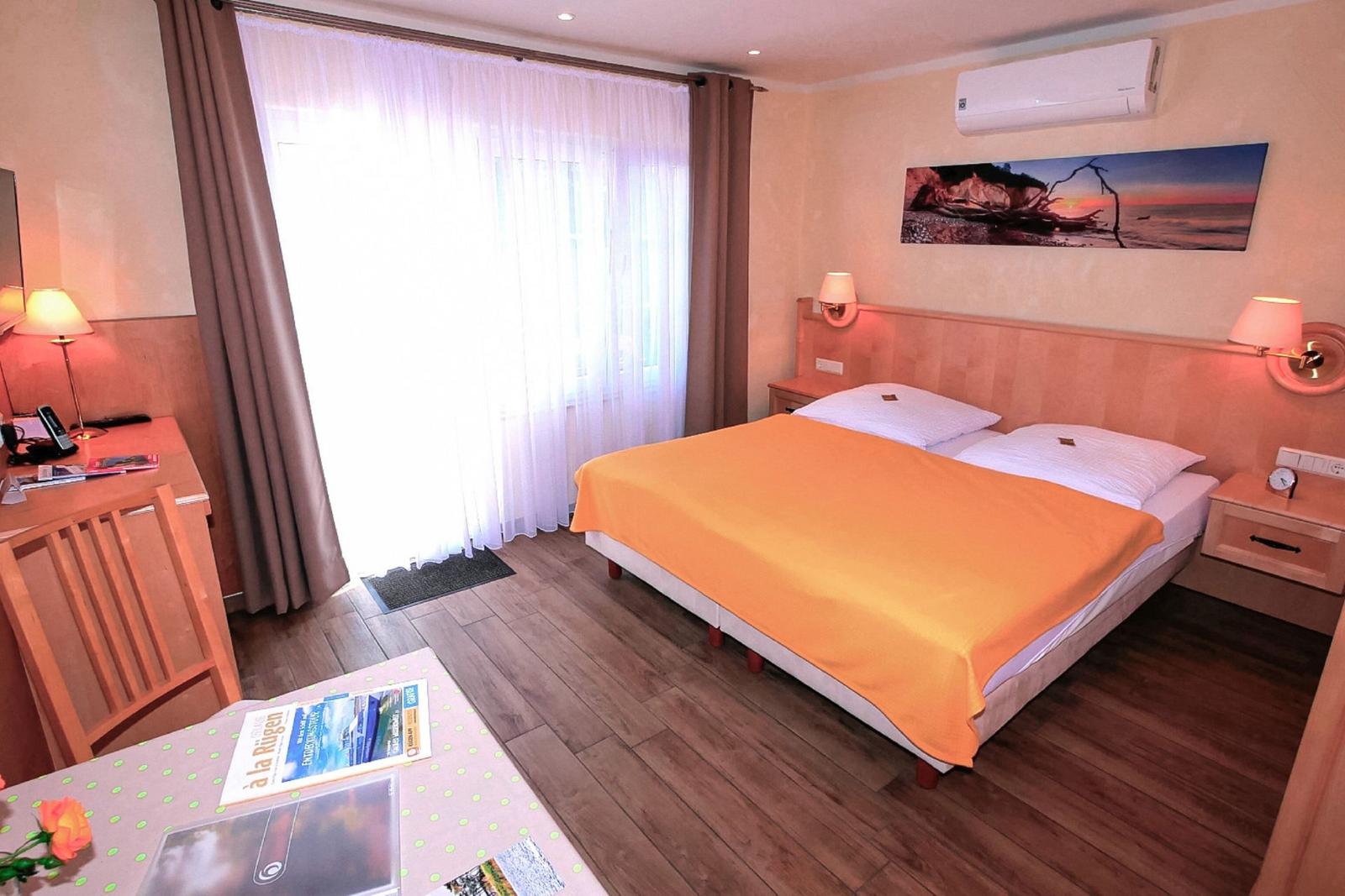 Schlafzimmer mit Doppelbett, Schreibtisch und großen Fenstern mit Vorhängen.