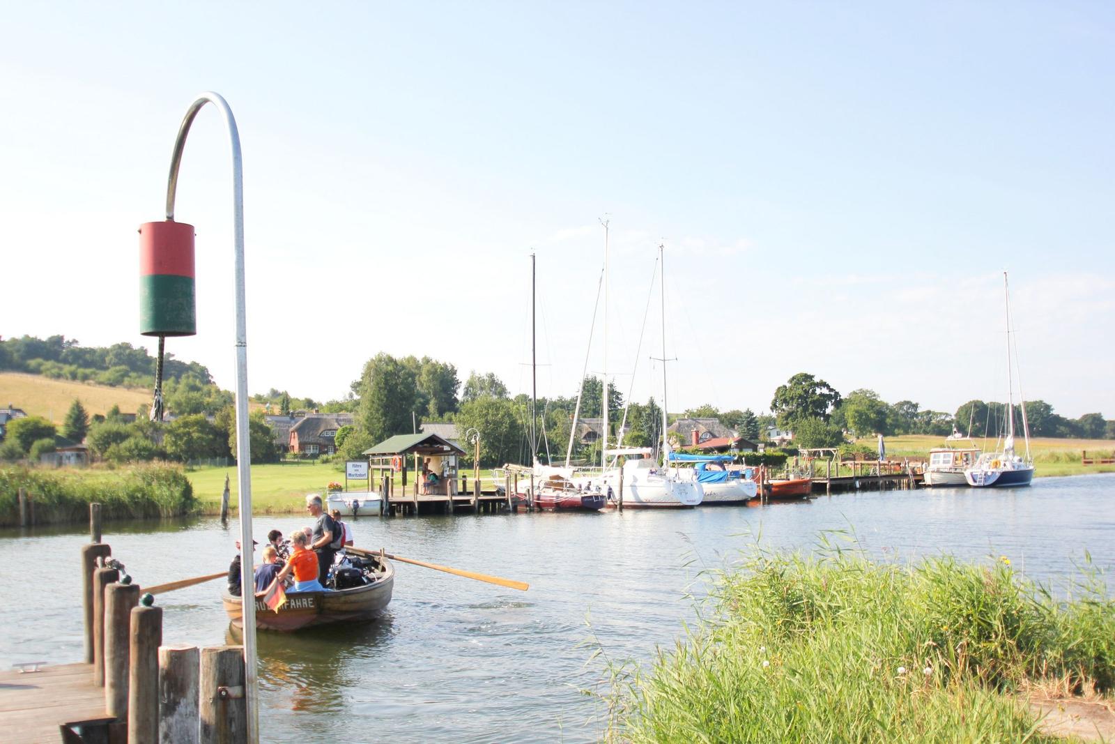 Boot fährt auf Fluss, Segelboote liegen am Ufer