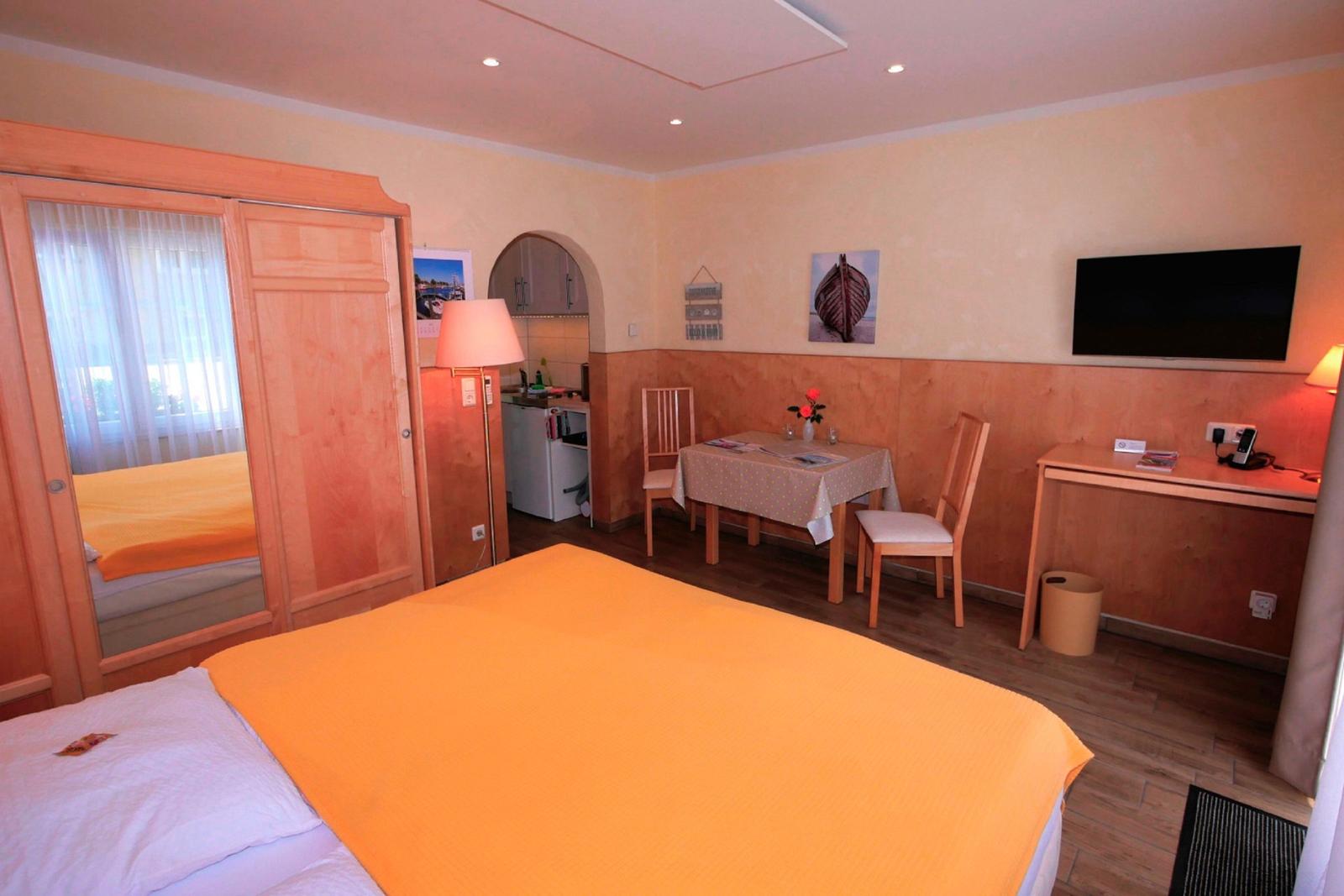 Ein Schlafzimmer mit Bett, Schreibtisch, Tisch mit Stühlen und Fernseher an der Wand.