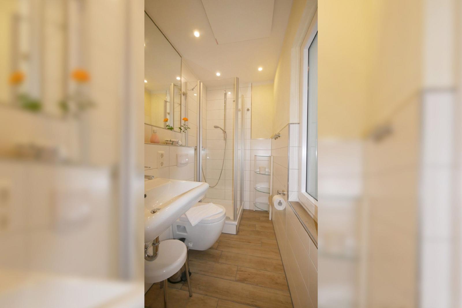 Badezimmer mit Dusche, WC und Waschbecken. Holzfußboden und Fenster.