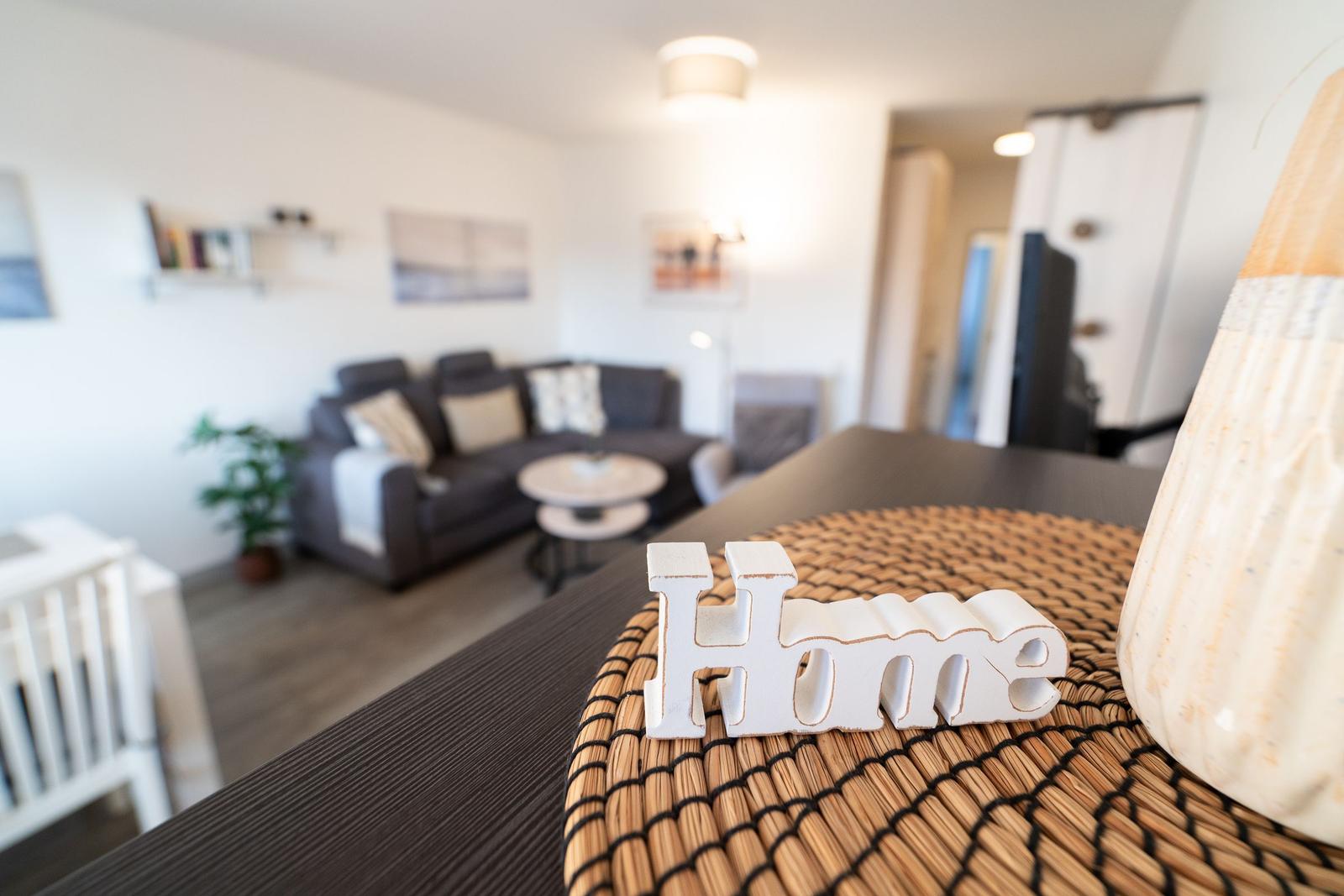 Ein Wohnzimmer mit Sofa, Tisch und Dekoration. Auf dem Tisch steht das Wort Home.