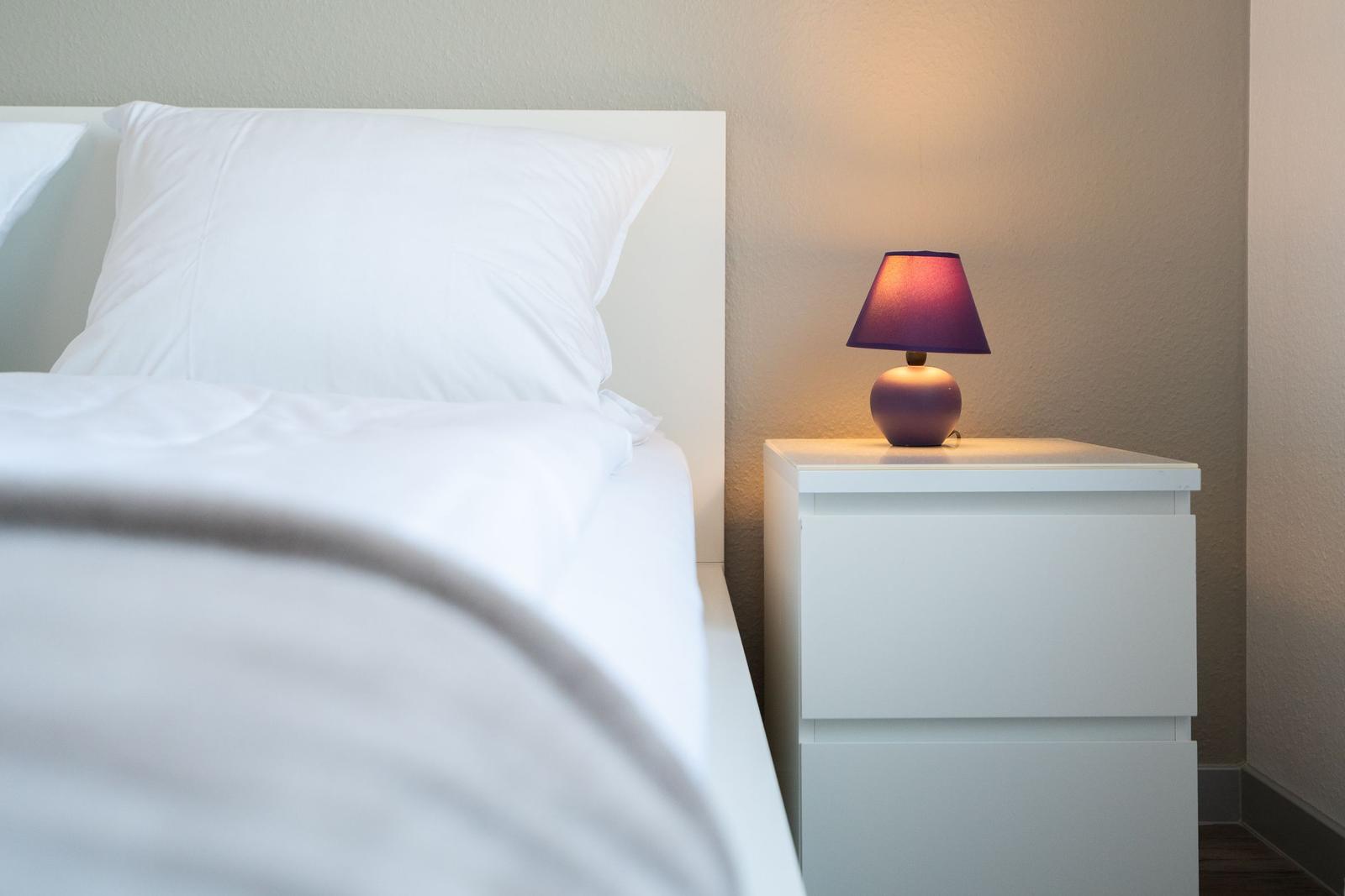 Ein Bett mit weißer Bettwäsche und einem Nachttisch mit einer Lampe.