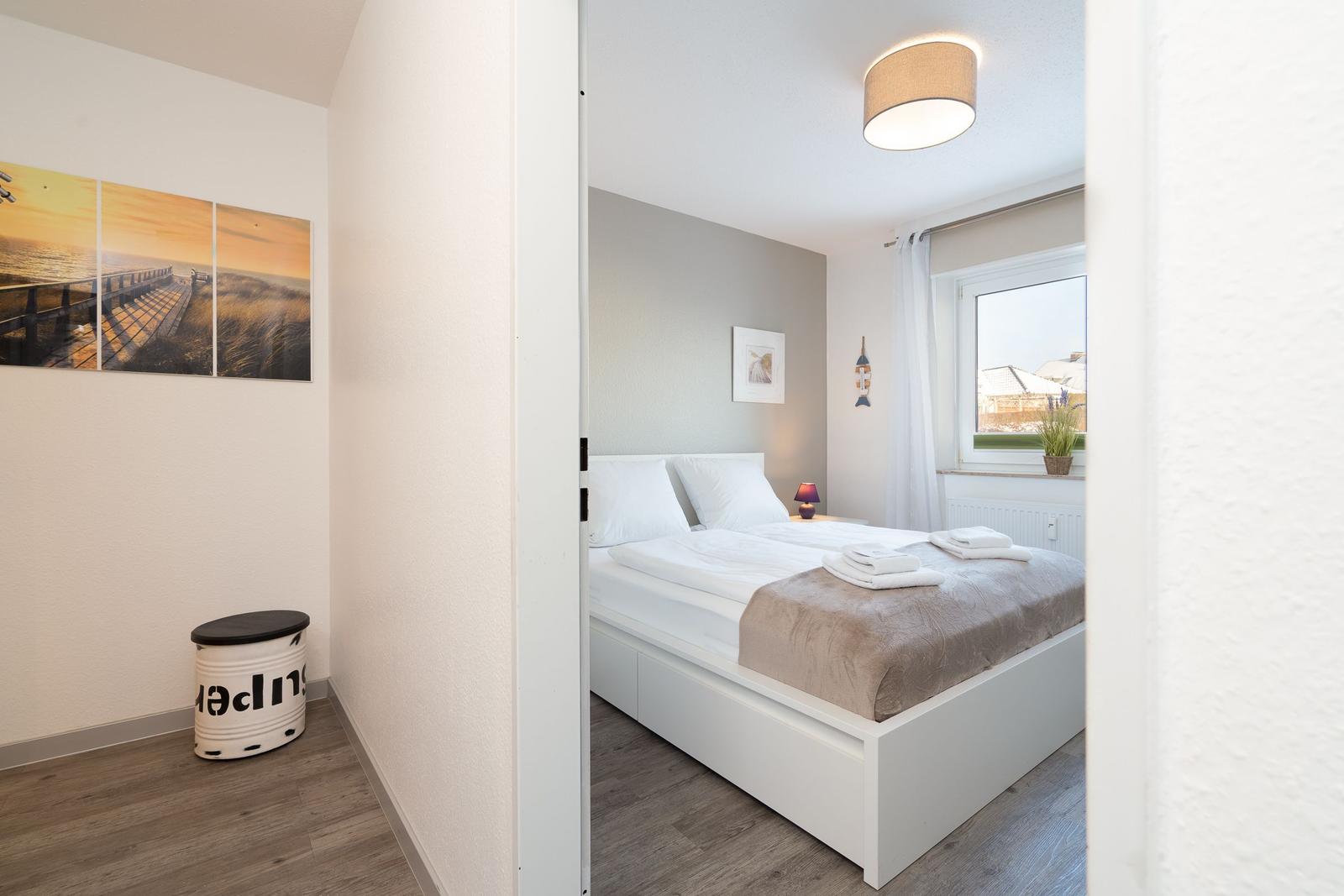 Schlafzimmer mit Doppelbett, Fenster und Wandbild. Flur mit Stuhl und Wandbild.