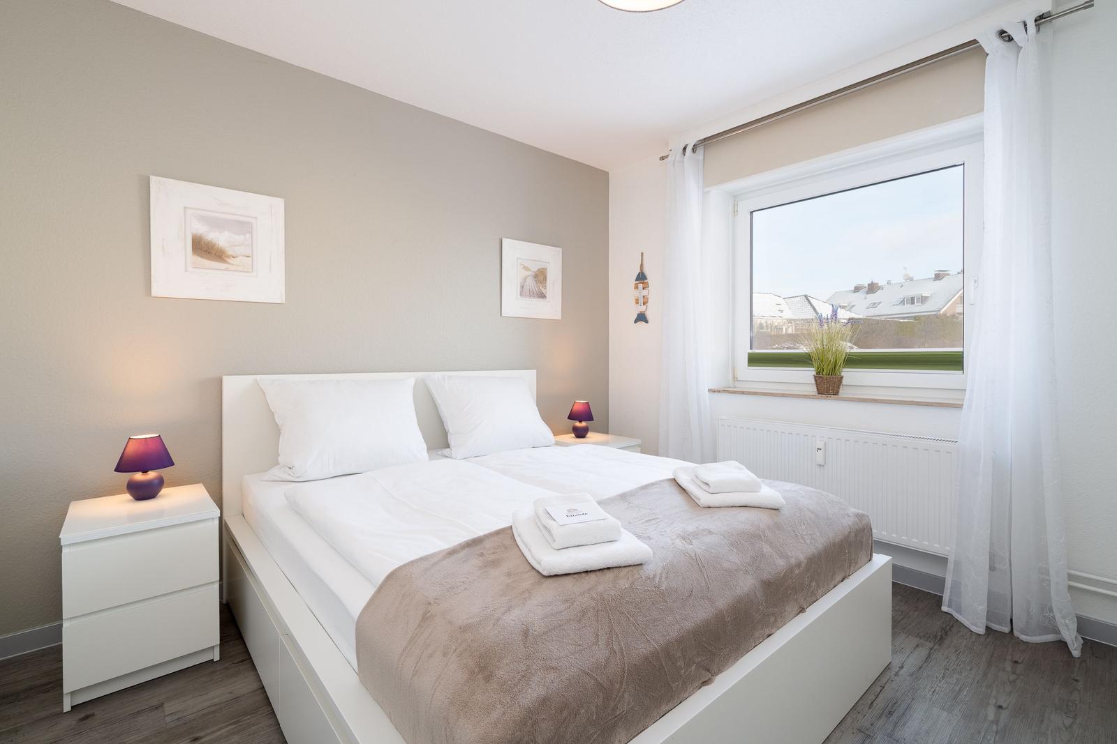 Schlafzimmer mit Doppelbett, Fenster und Nachttischen.