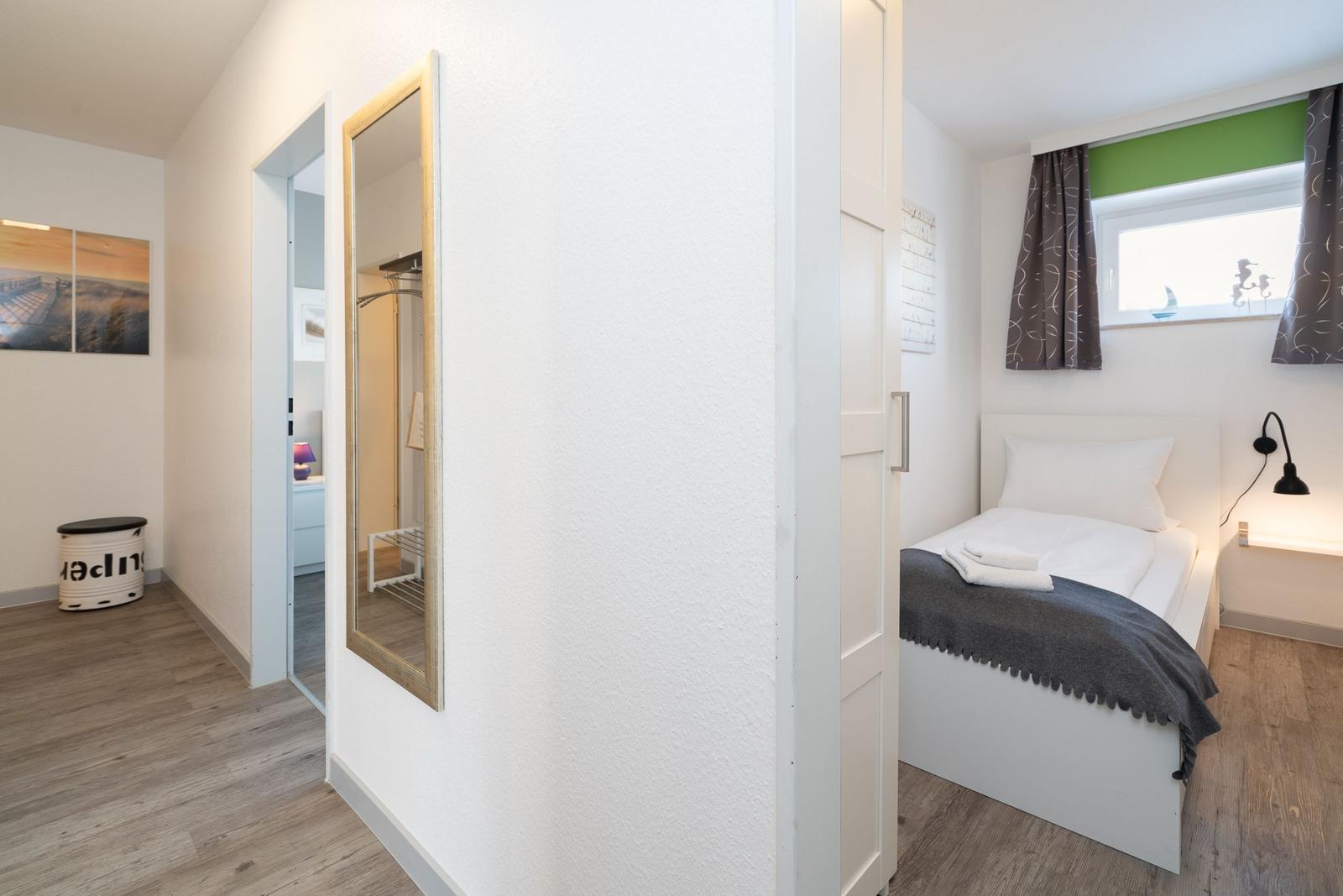 Schlafzimmer mit Bett, Fenster und Spiegel. Flur mit Wandbild und Aufbewahrungsbox.
