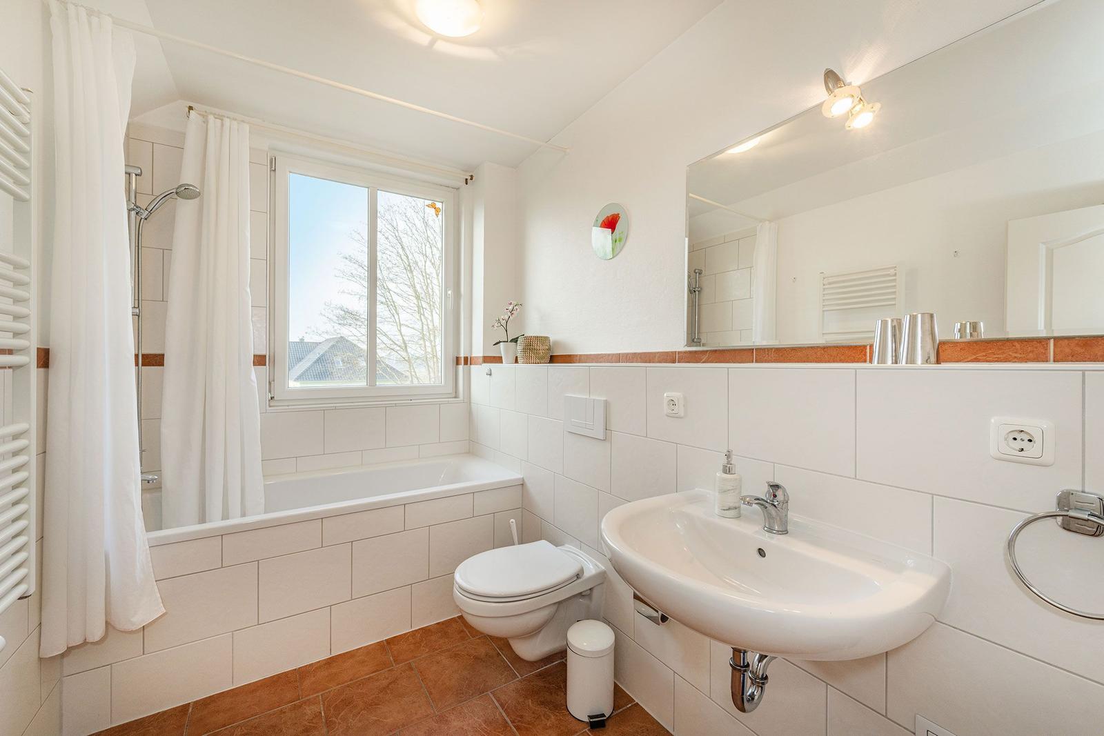 Badezimmer mit Badewanne, Dusche, Waschbecken und Toilette. Fenster mit Blick nach draußen.