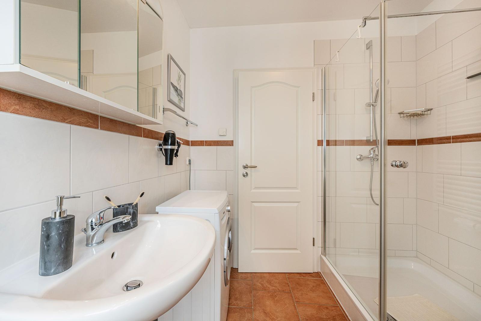 Badezimmer mit Dusche, Waschmaschine und Spiegelschrank.