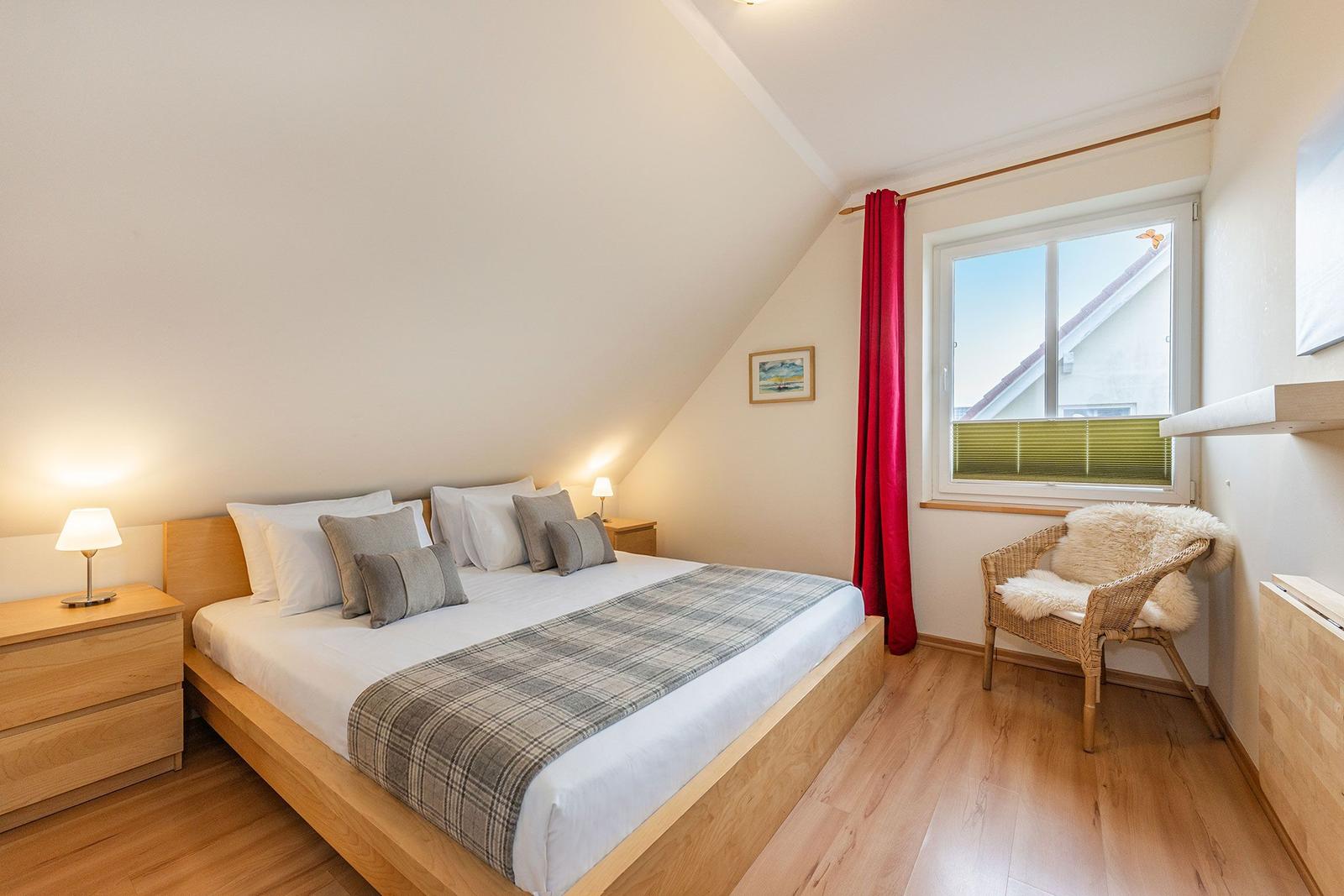 Schlafzimmer mit Dachschrägen, Bett, Nachttisch, Stuhl und Fenster.