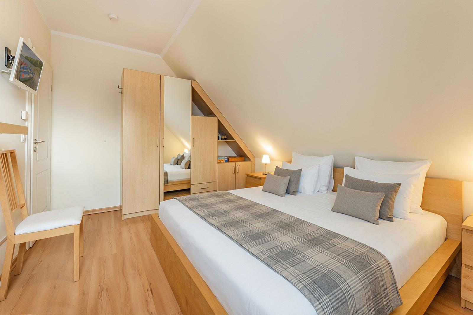 Schlafzimmer mit Doppelbett, Kleiderschrank und Fernseher an der Wand.