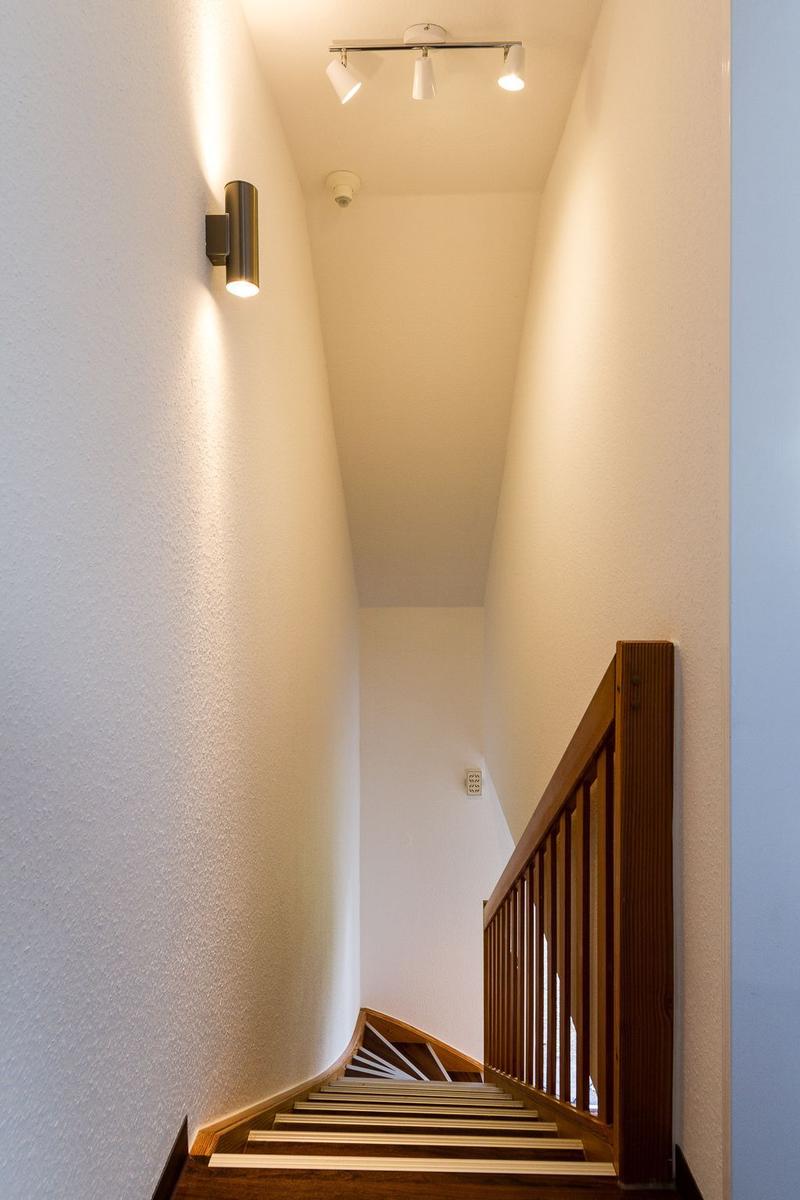 Helle Treppe mit Holzgeländer und moderner Beleuchtung an den Wänden.