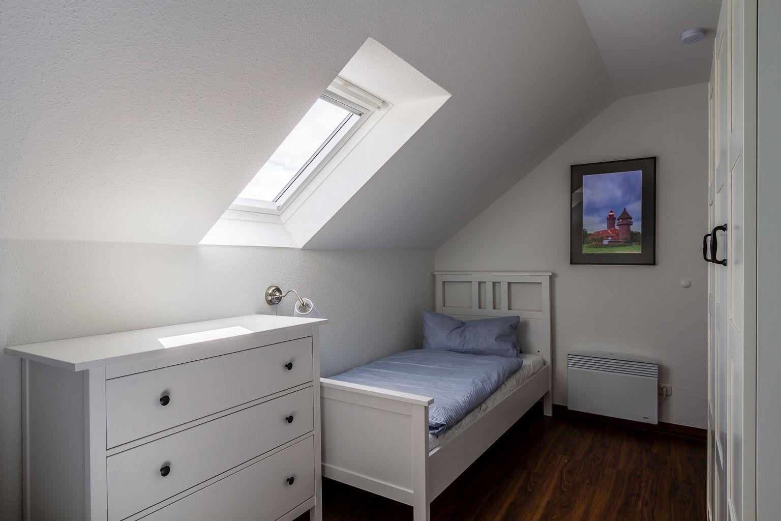 Schlafzimmer mit Dachschrägen, Dachfenster, weißem Bett und Kleiderschrank.