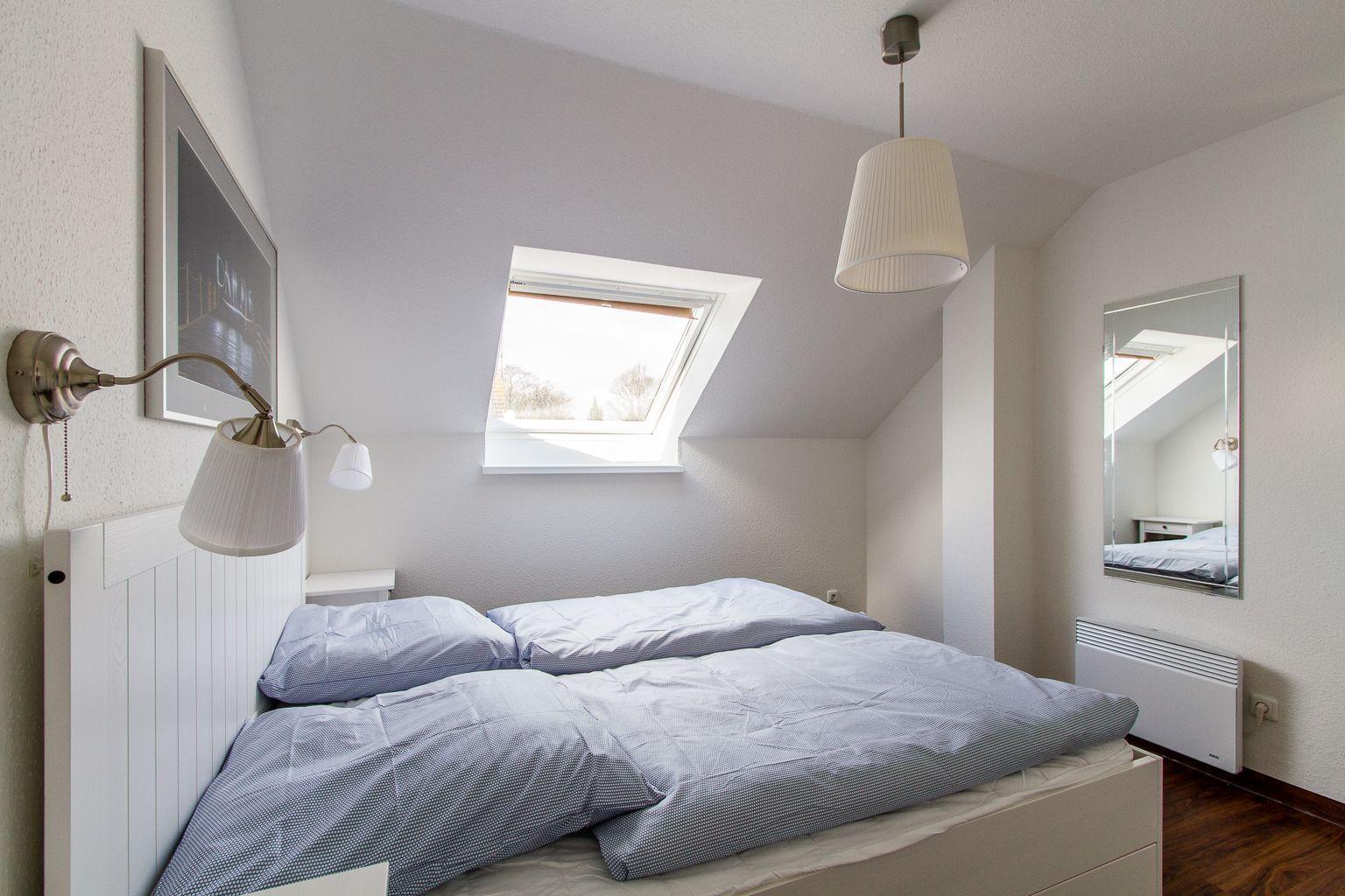 Schlafzimmer mit Dachfenster, Bett, Spiegel und Deckenleuchte.