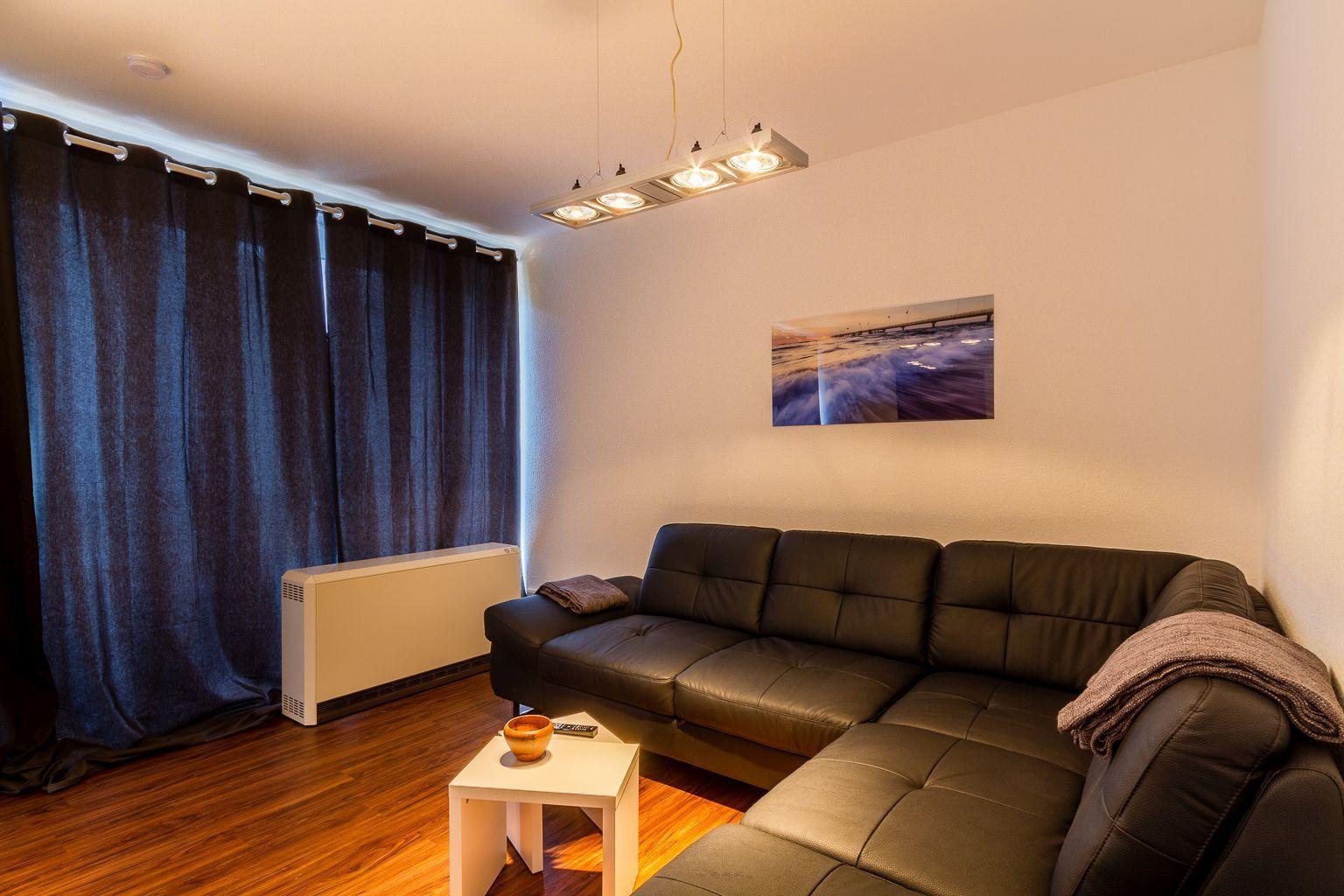Wohnzimmer mit Leder Sofa, Tisch, Wandbild und Vorhängen.