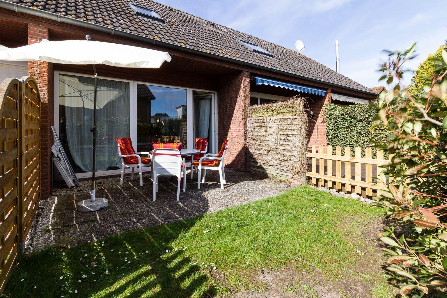 Hinterhof mit Sitzgruppe, Sonnenschirm und Grasfläche. Holzzaun und Kletterpflanzen umgeben den Bereich.
