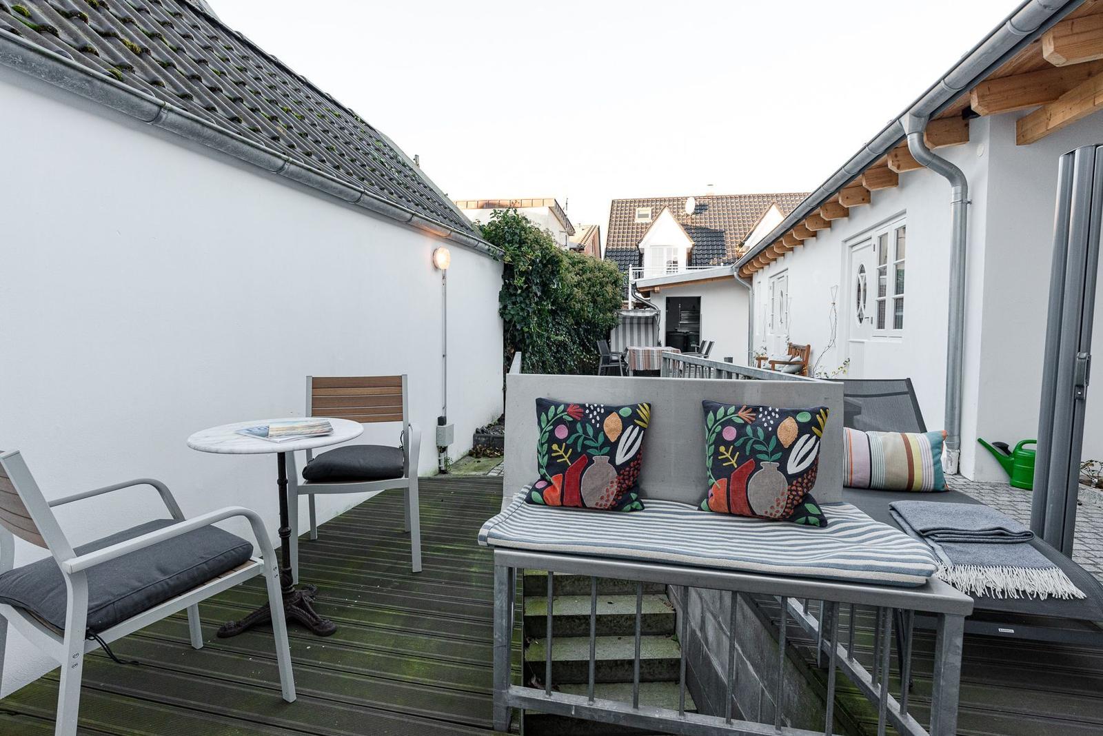 Terrasse mit Sitzgelegenheit, Tisch und Stühlen. Hintergrund: weiße Wände und Dächer.