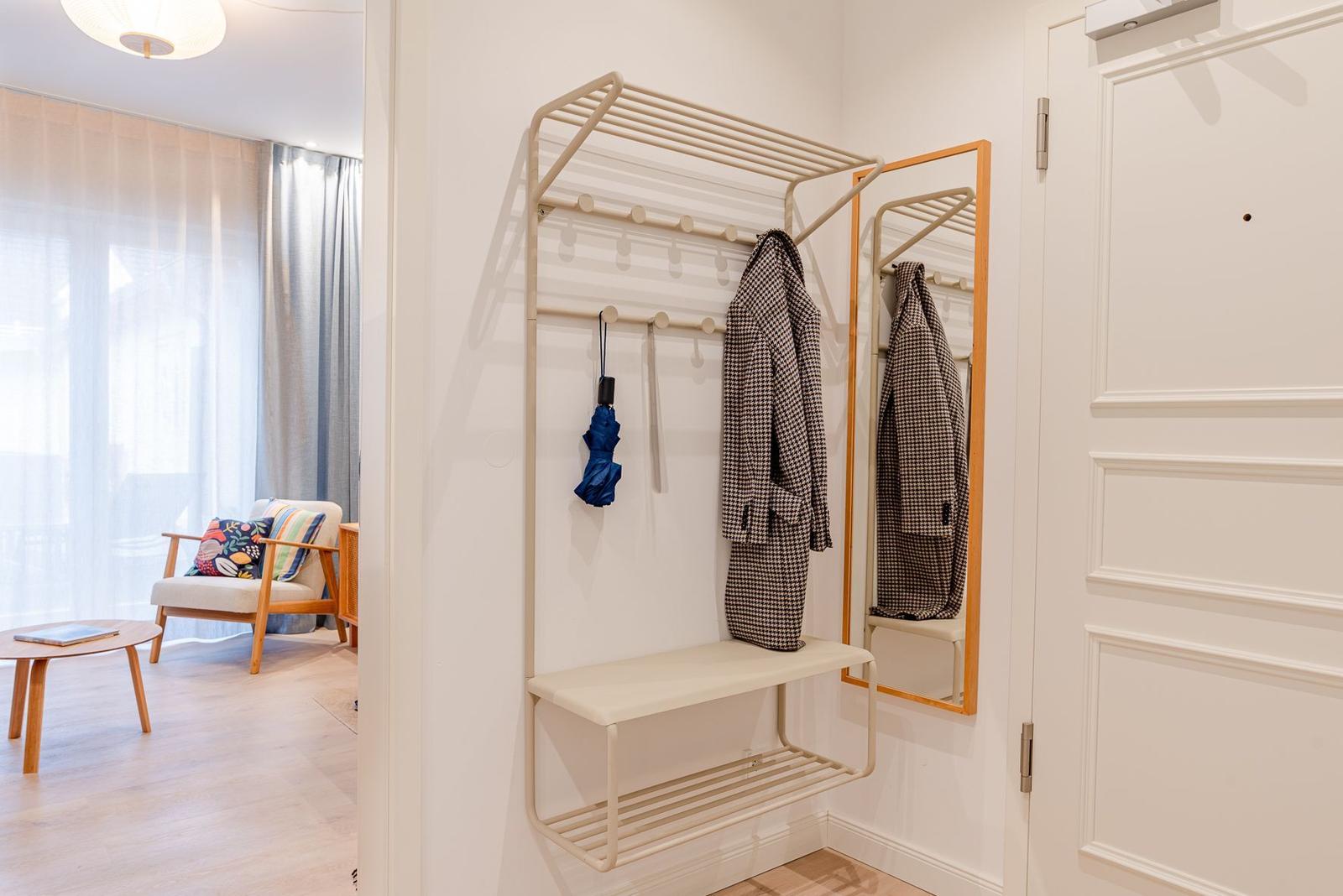 Eingangsbereich mit Garderobe, Spiegel und Sitzbank. Im Hintergrund ist ein Wohnbereich mit Sessel und Tisch.