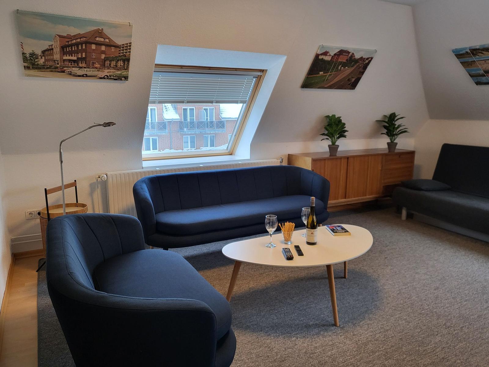 Wohnzimmer mit blauer Couch, Tisch und Dachfenster. Wandbilder und Pflanzen.