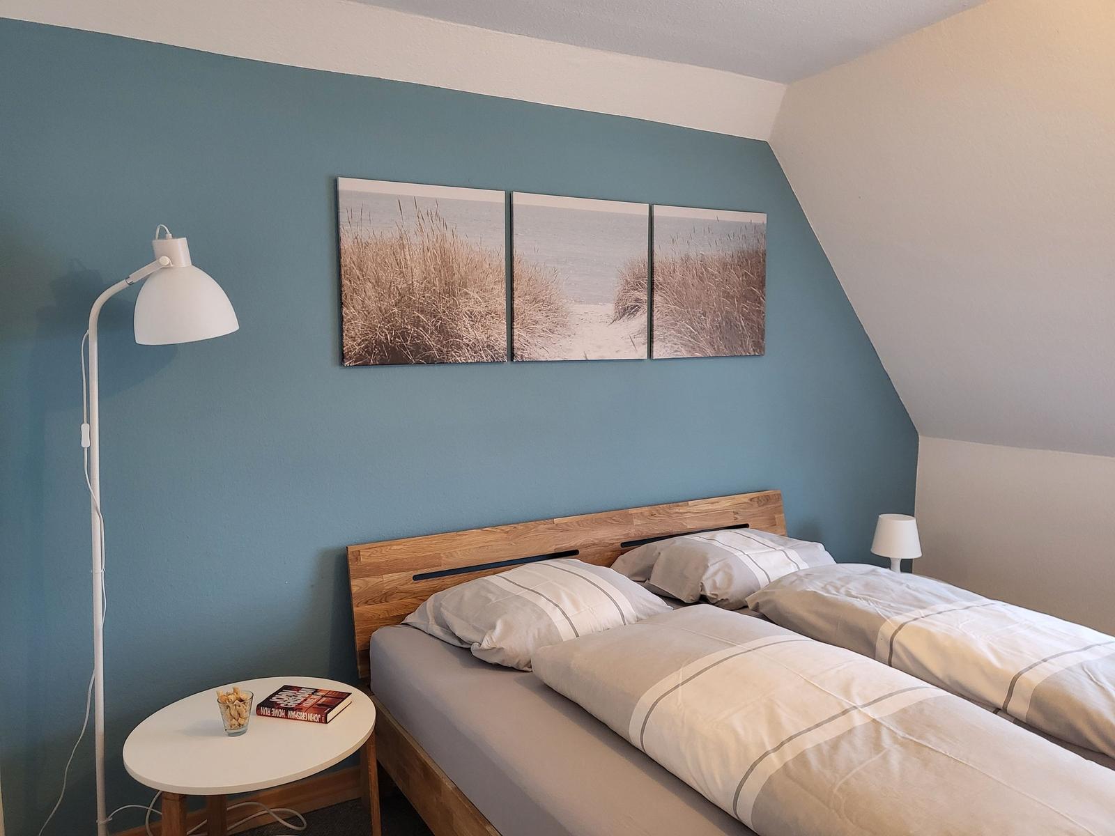 Schlafzimmer mit Doppelbett, Wandbild und Stehlampe.