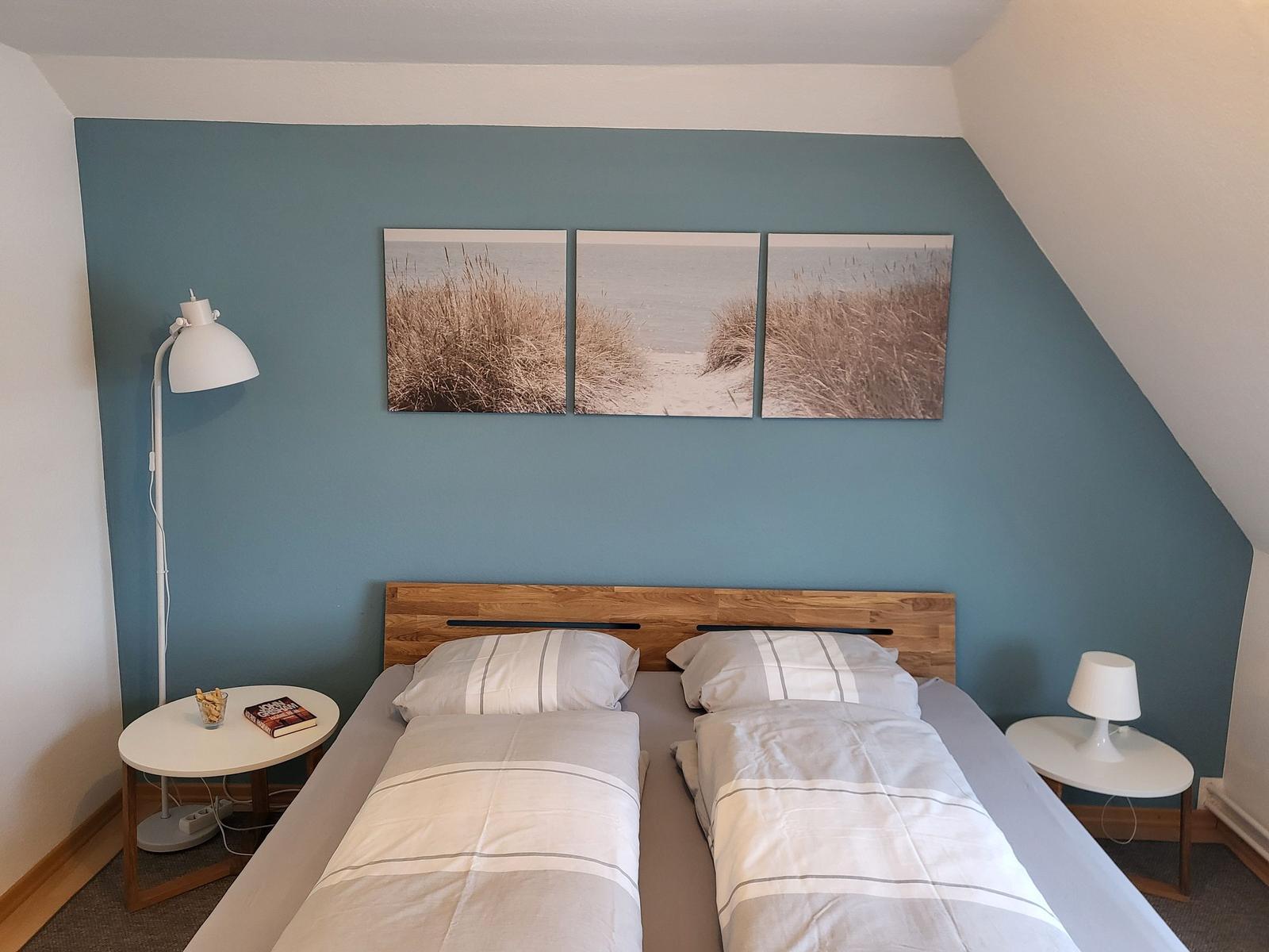 Schlafzimmer mit Doppelbett, blauer Wand und drei Strandbildern.