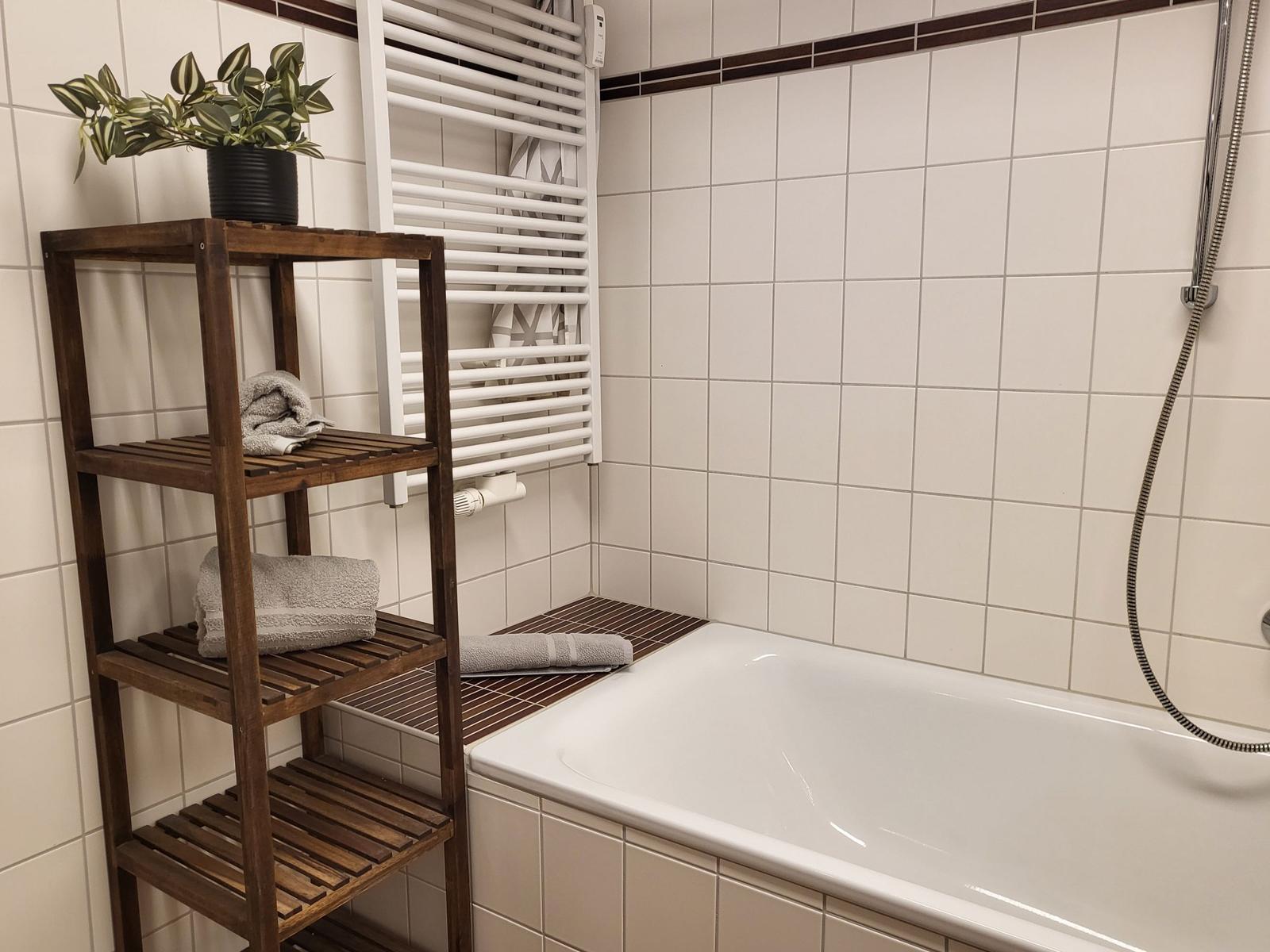 Badezimmer mit Badewanne, Holzregal und Heizkörper an der Wand.