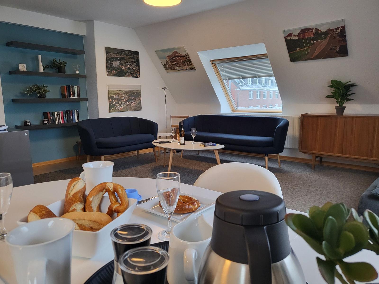 Wohnbereich mit zwei dunkelblauen Sofas, Tisch und Blick auf Dachfenster.