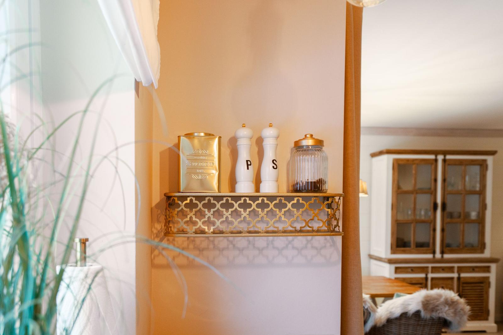 Goldschale mit Salz- und Pfeffermühle, Zuckerdose und Kaffeefilter auf Wandregal.