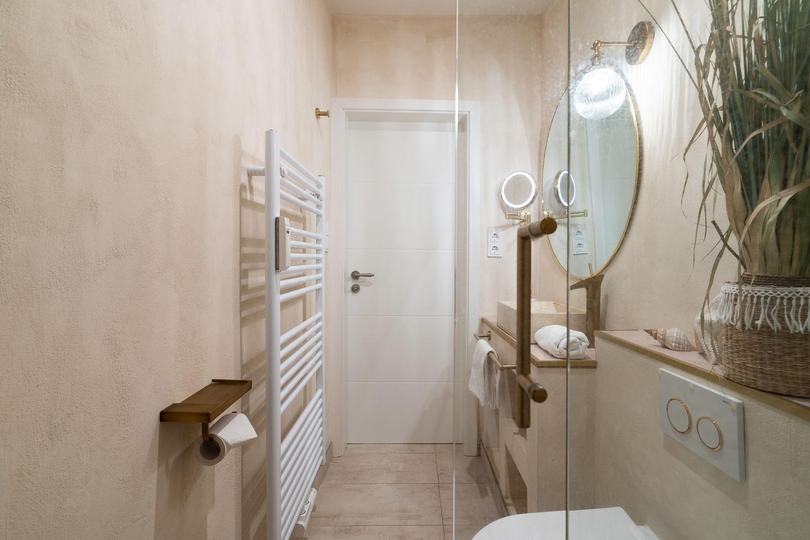 Badezimmer mit Dusche, Waschbecken und Heizung. Spiegel und Pflanze sind sichtbar.