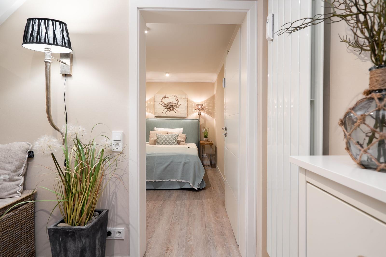 Schlafzimmer mit Bett, Wandbild und Holzboden. Flur mit Pflanzen und Lampen.
