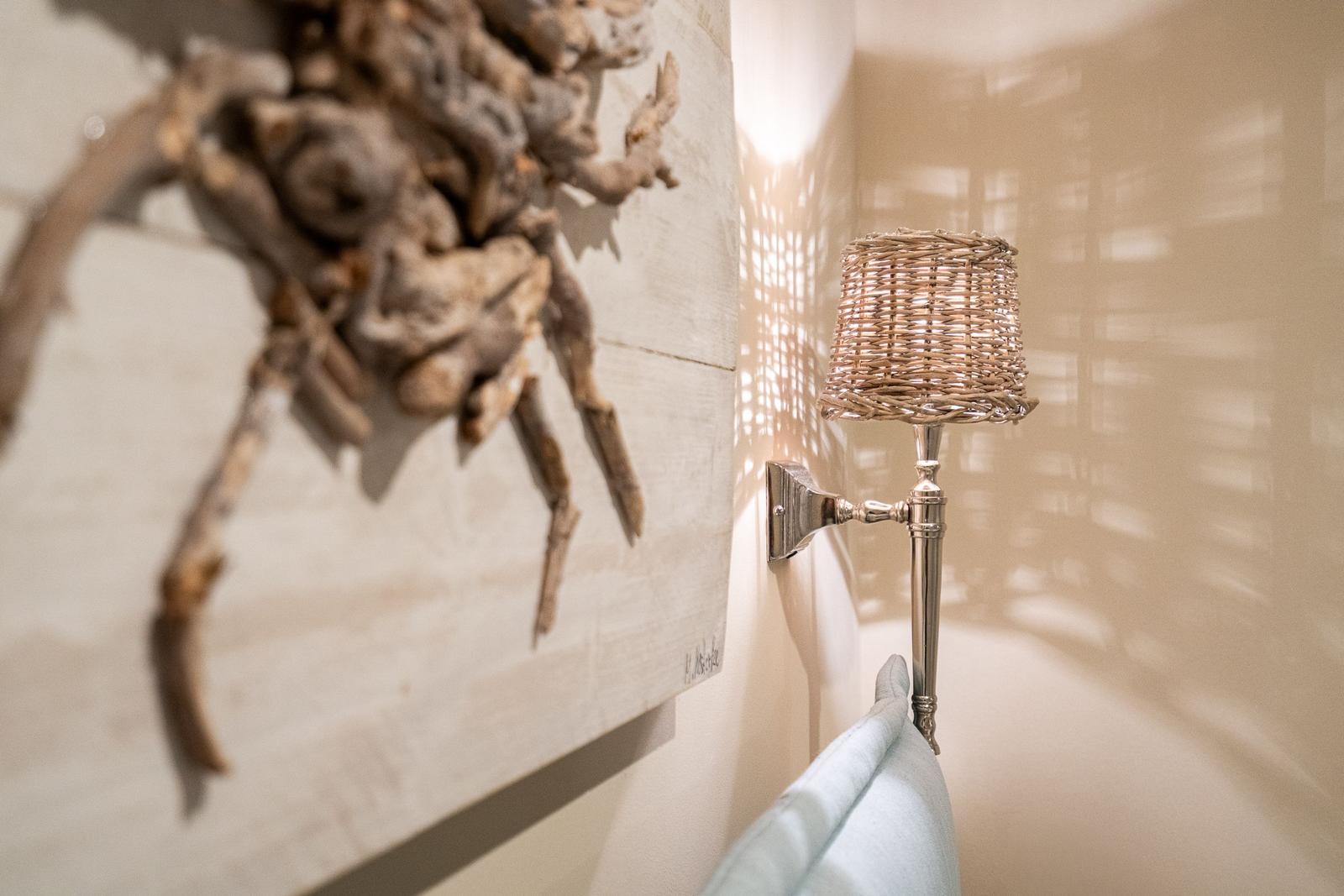 Wandlampe mit geflochtenem Schirm neben einer Wanddekoration aus Holz.
