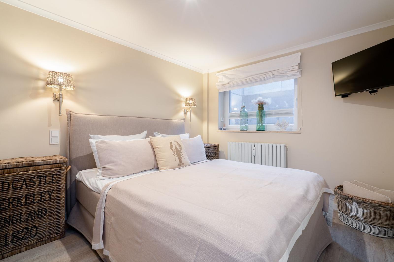 Schlafzimmer mit Bett, Fenster, Wandlampe und Fernseher.