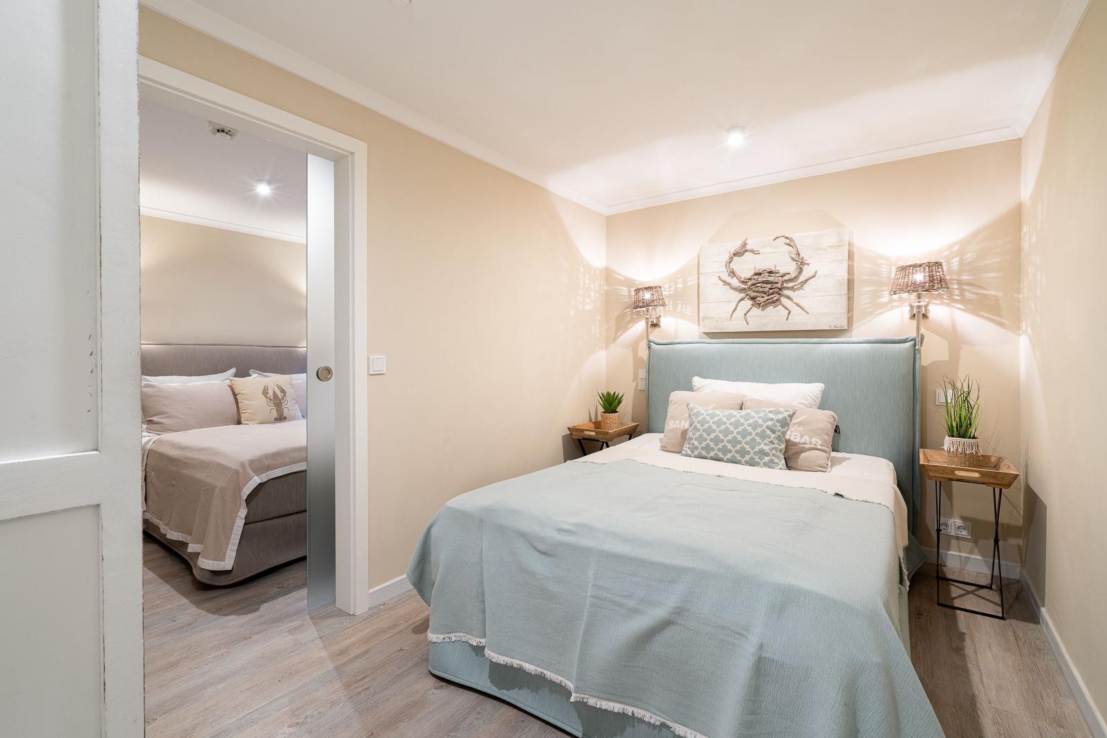 Schlafzimmer mit Bett, Wandbild und Nachttischen. Durchgang zu weiterem Schlafzimmer.