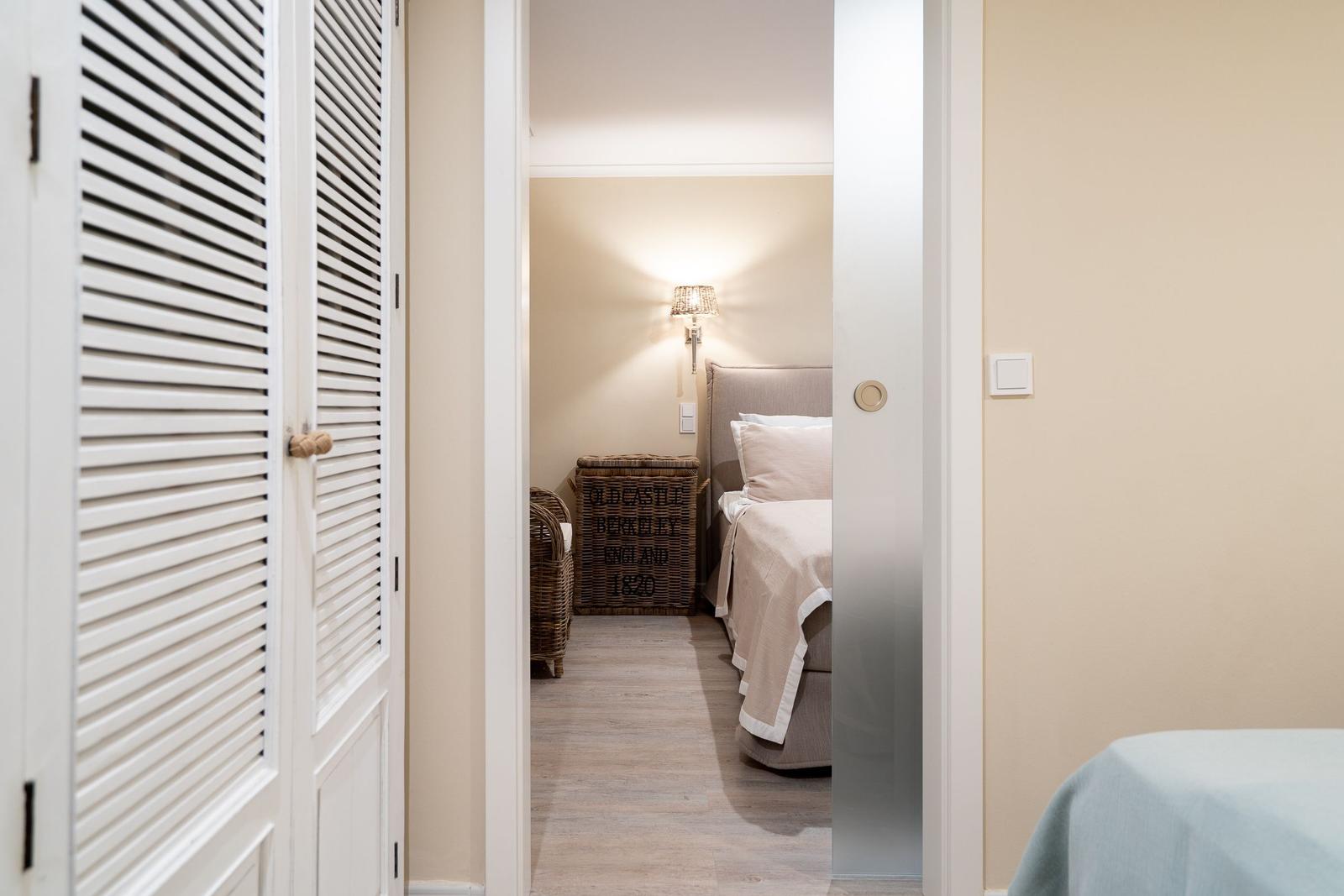 Schlafzimmer mit Bett, Wandleuchte und Korb. Blick durch Tür mit Schiebetüren.