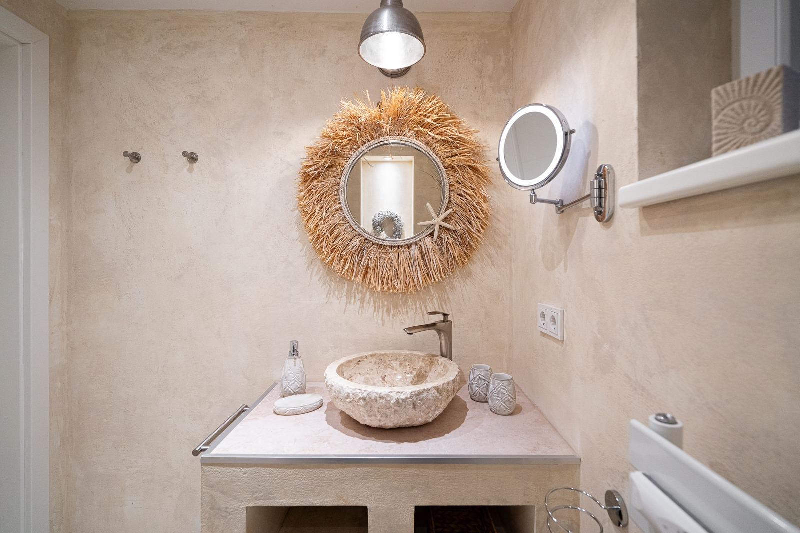Badezimmer mit Steinwaschbecken, runden Spiegel und Wandhalterungen.