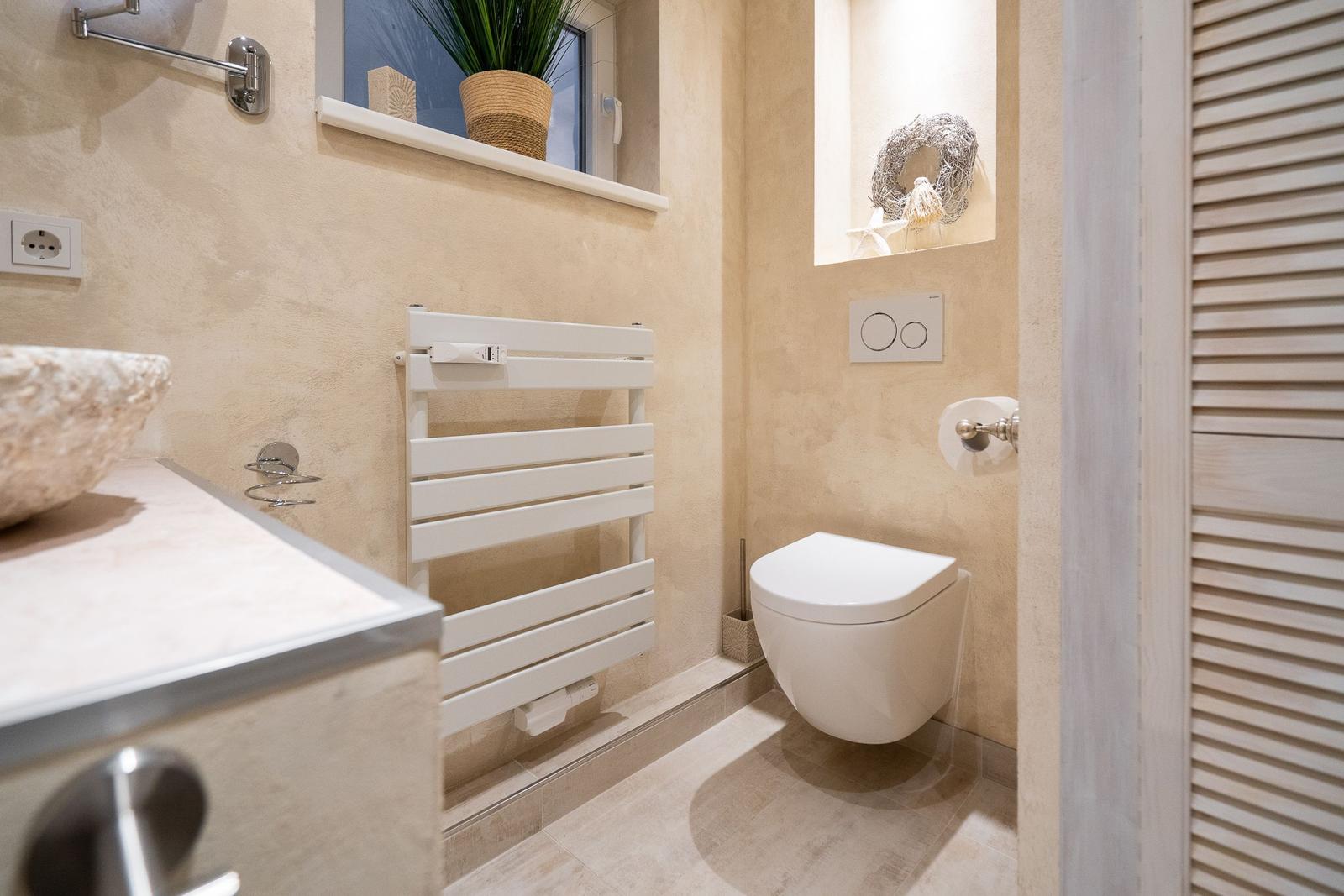 Bad mit Toilette, Heizkörper und Waschtisch. Fenster mit Pflanze und dekorativer Nische.