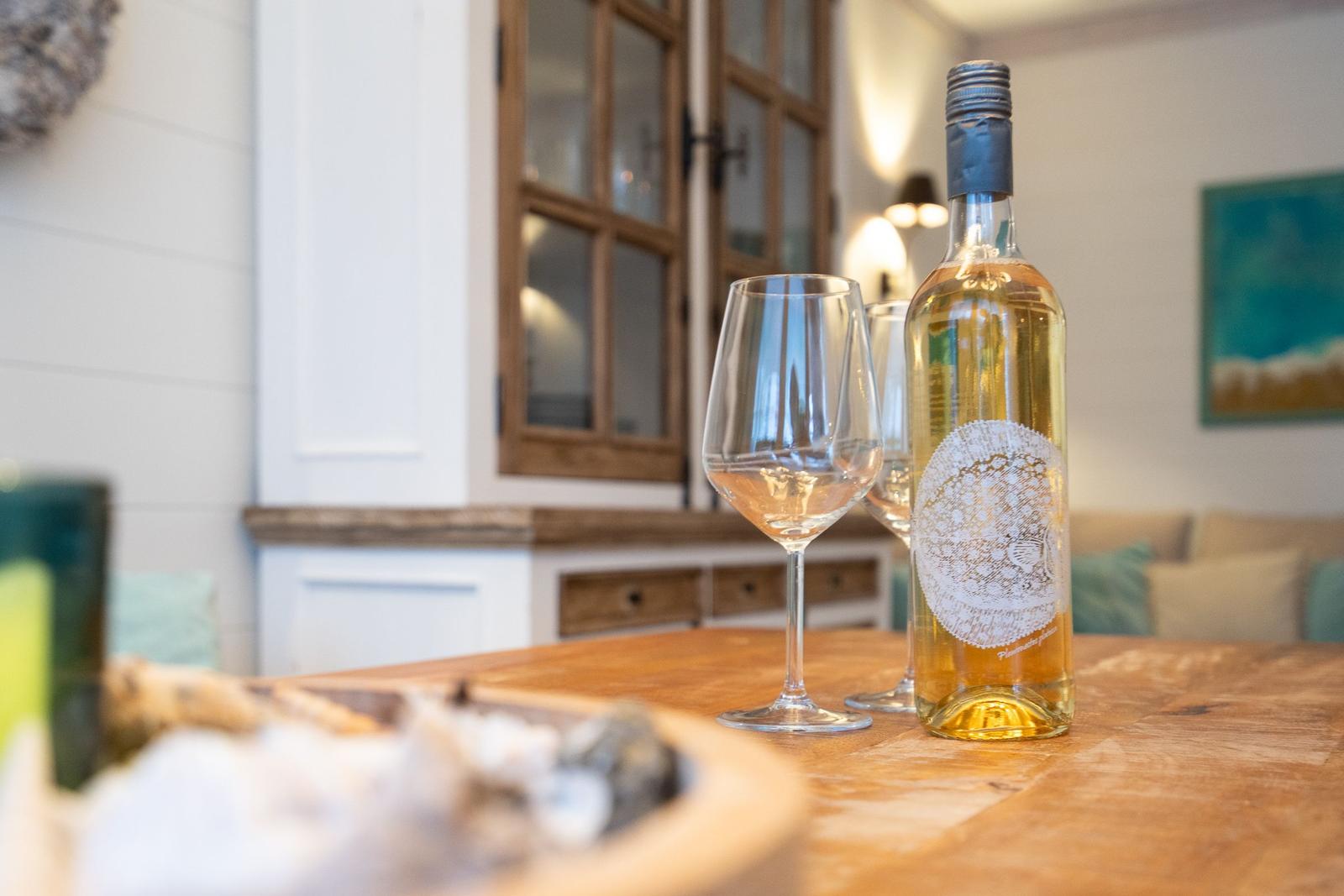 Ein Tisch mit einer Weinflasche und zwei Gläsern. Im Hintergrund ein Wohnbereich mit Holzmöbeln.