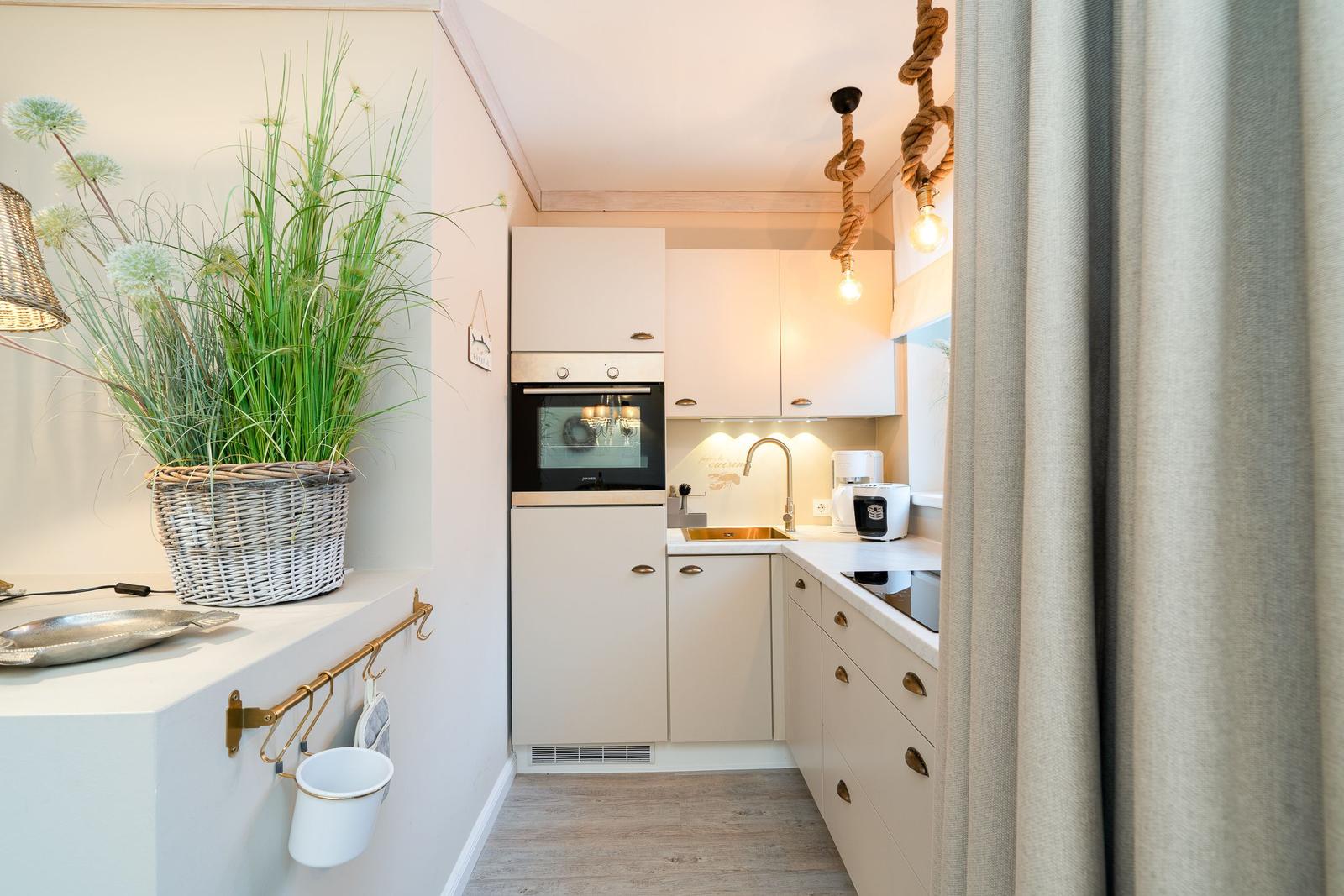 Küche mit weißen Schränken, Edelstahlspüle und Seilbeleuchtung.