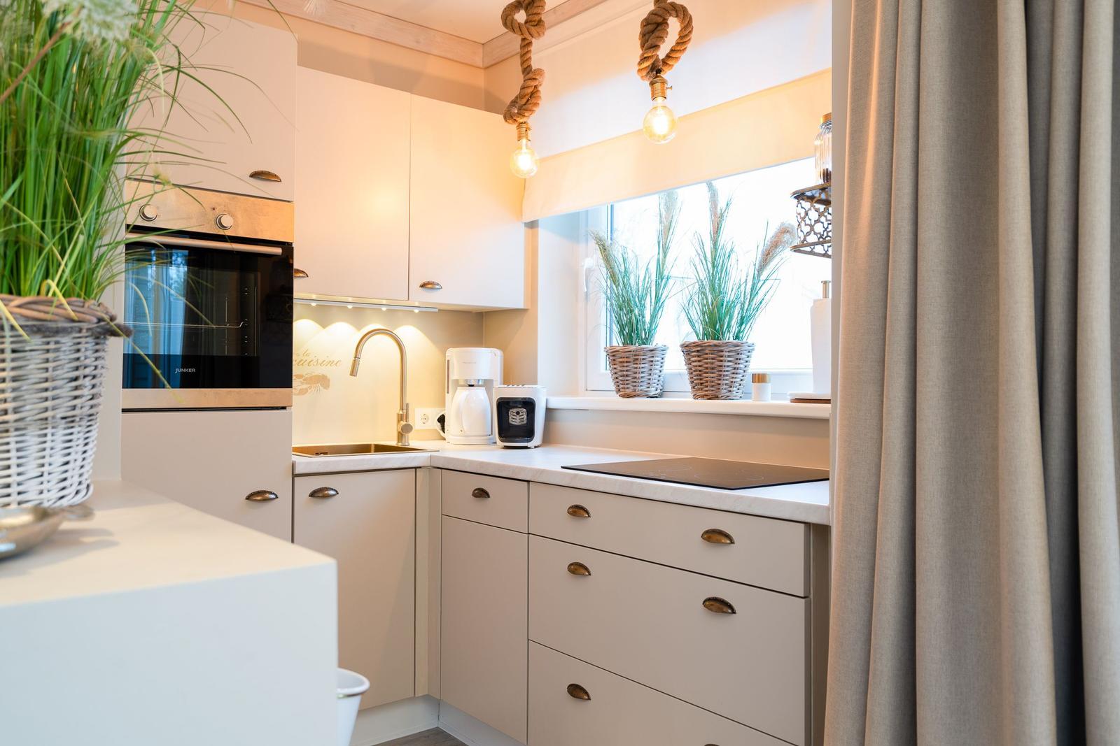 Küche mit weißen Schränken, Herd und Fenster mit Pflanzen.