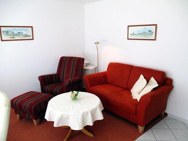 Wohnzimmer mit rotem Sofa, gestreifter Sessel und runden Tisch mit Tischdecke.