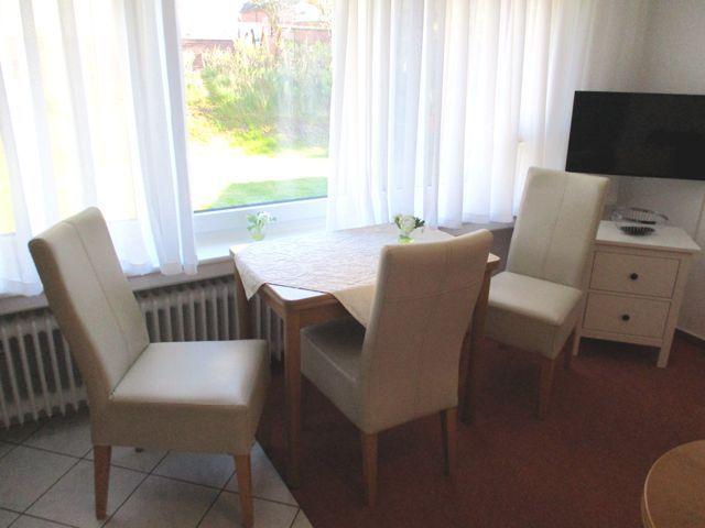 Esszimmer mit Tisch, vier Stühlen, Fernseher und Fenster mit Blick auf Garten.
