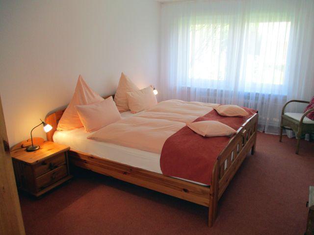 Ein Schlafzimmer mit Doppelbett, Holzrahmen, Nachttisch und Fenster mit Vorhängen.