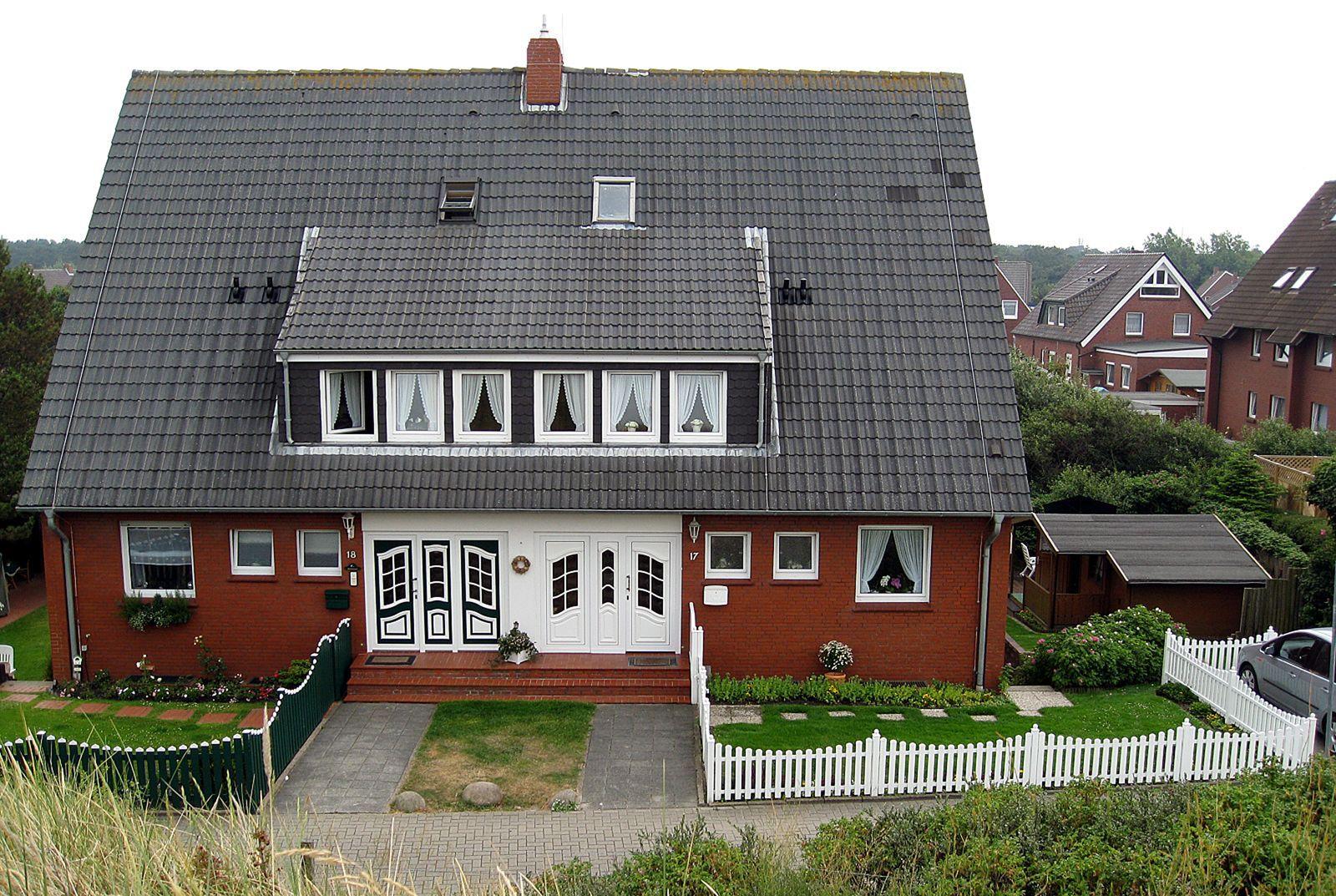 Rotes Haus mit grauem Dach, weißer Veranda und gepflegtem Vorgarten.