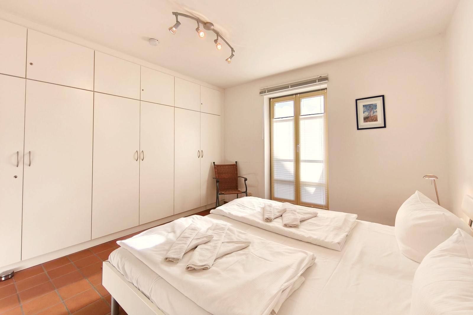 Schlafzimmer mit Doppelbett, Kleiderschrank und Fenster mit Jalousie.