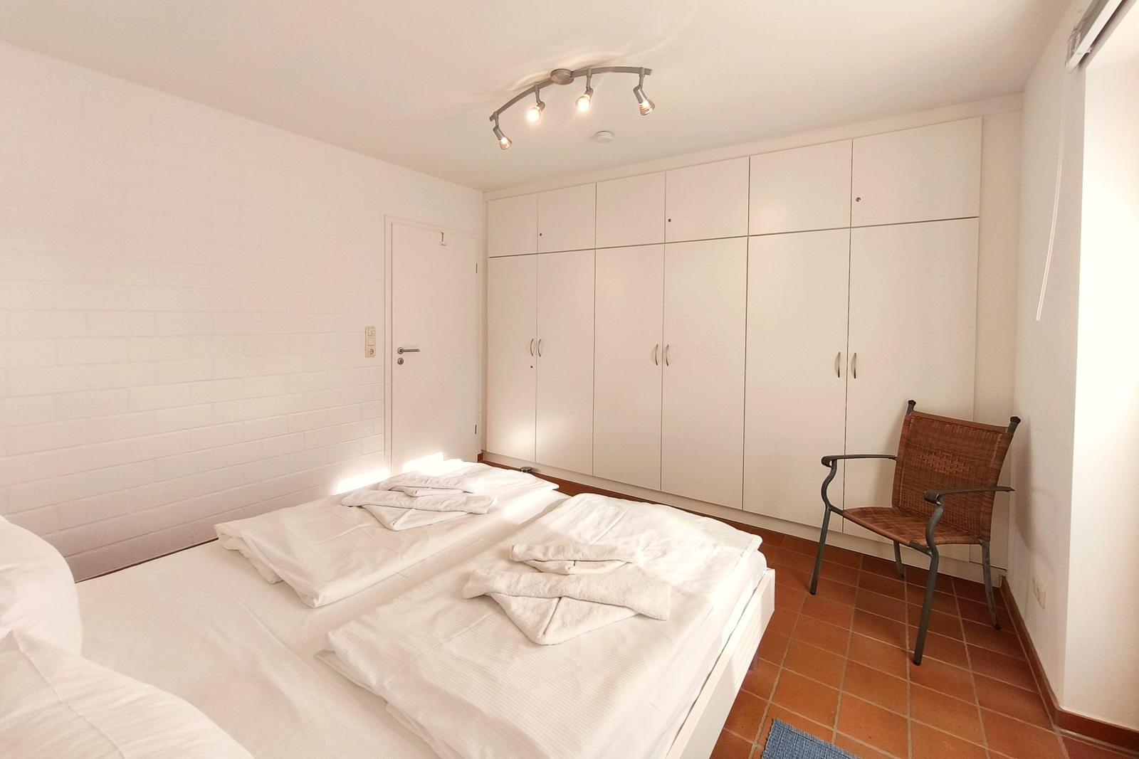 Schlafzimmer mit Doppelbett, weißen Schränken und einem Stuhl.