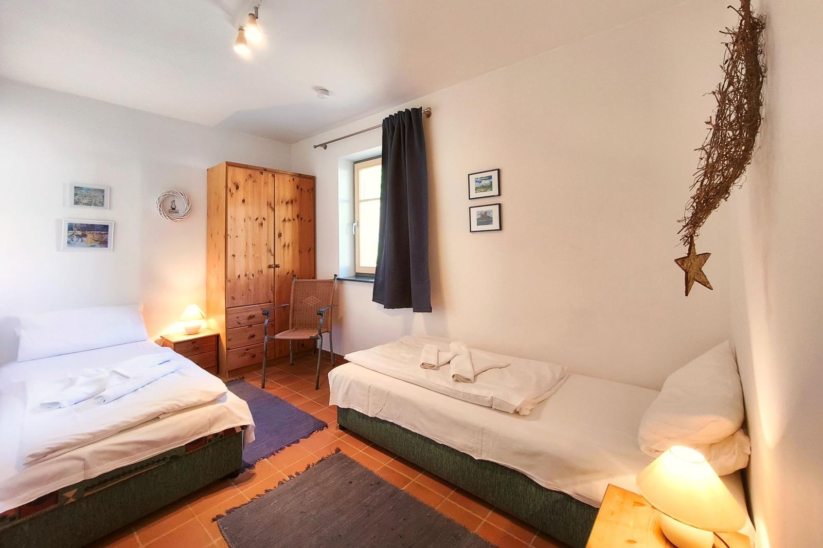 Zwei Betten, Holzschrank, Fenster mit Vorhang, Lampen und Wanddekoration.