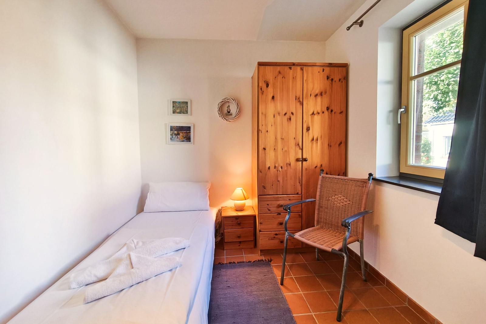 Ein Schlafzimmer mit einem Bett, einem Holzschrank, einem Stuhl und einem Fenster.