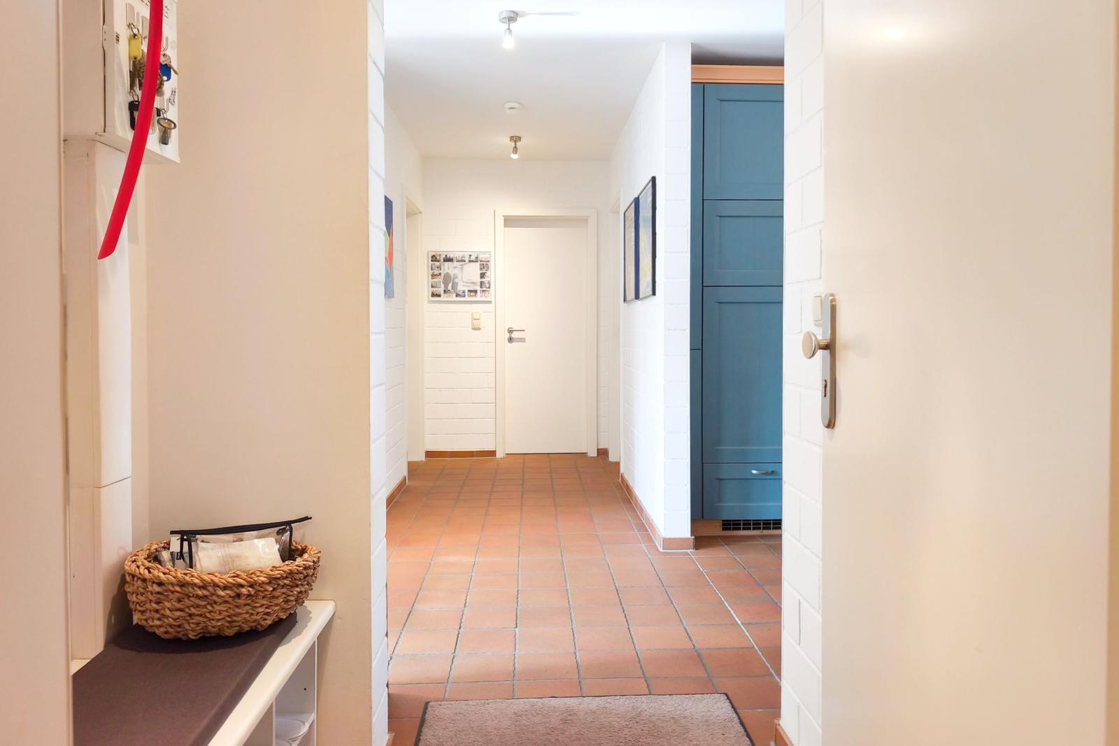 Flur mit Terrakottboden, blauer Schrank und Wandbildern