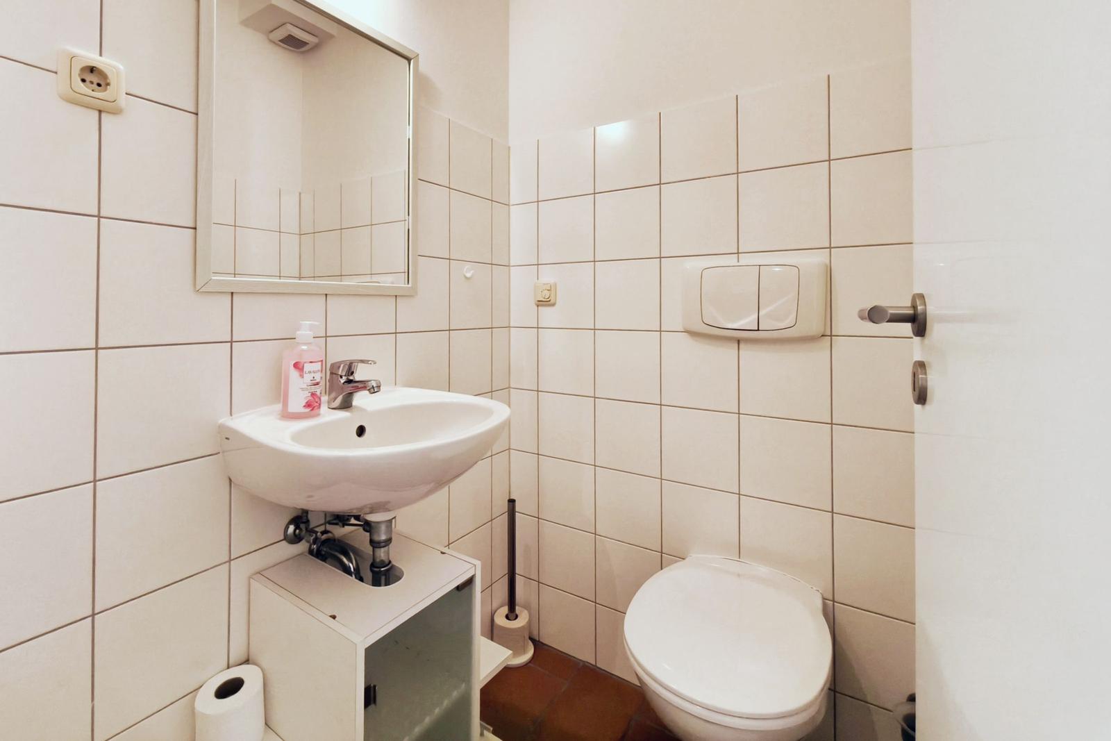 Badezimmer mit Waschbecken, Spiegel, Toilette und Toilettenpapier