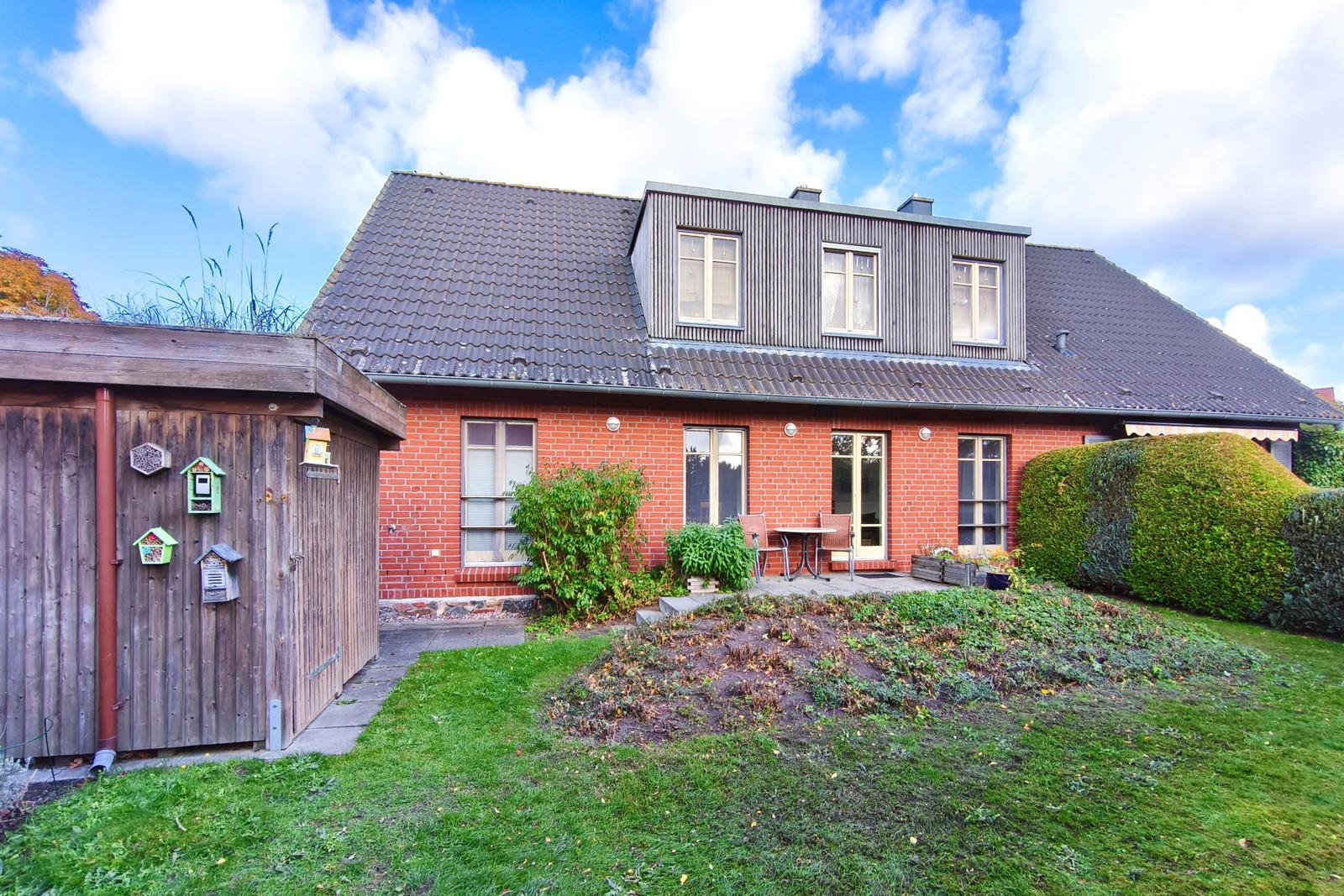 Rotes Backsteingebäude mit Terrasse und Garten. Holzgarage mit Vogelhäusern.