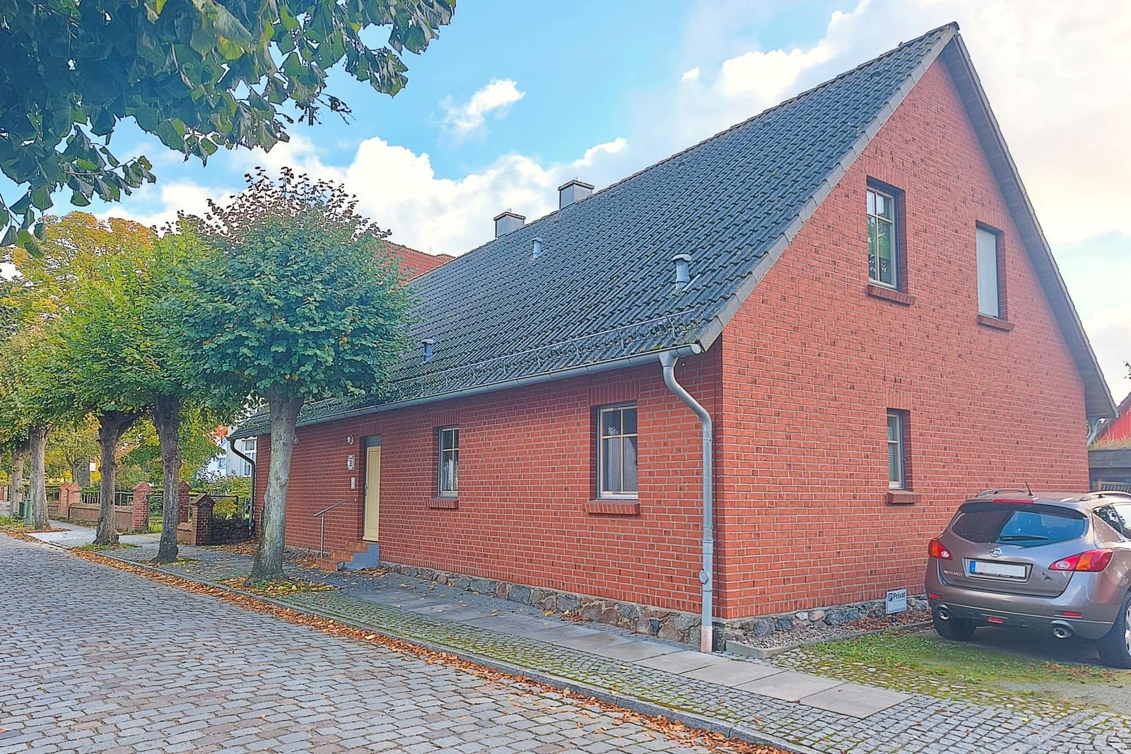 Rotes Backsteinhaus mit schwarzem Dach, Eingangstür und parkendem Auto.